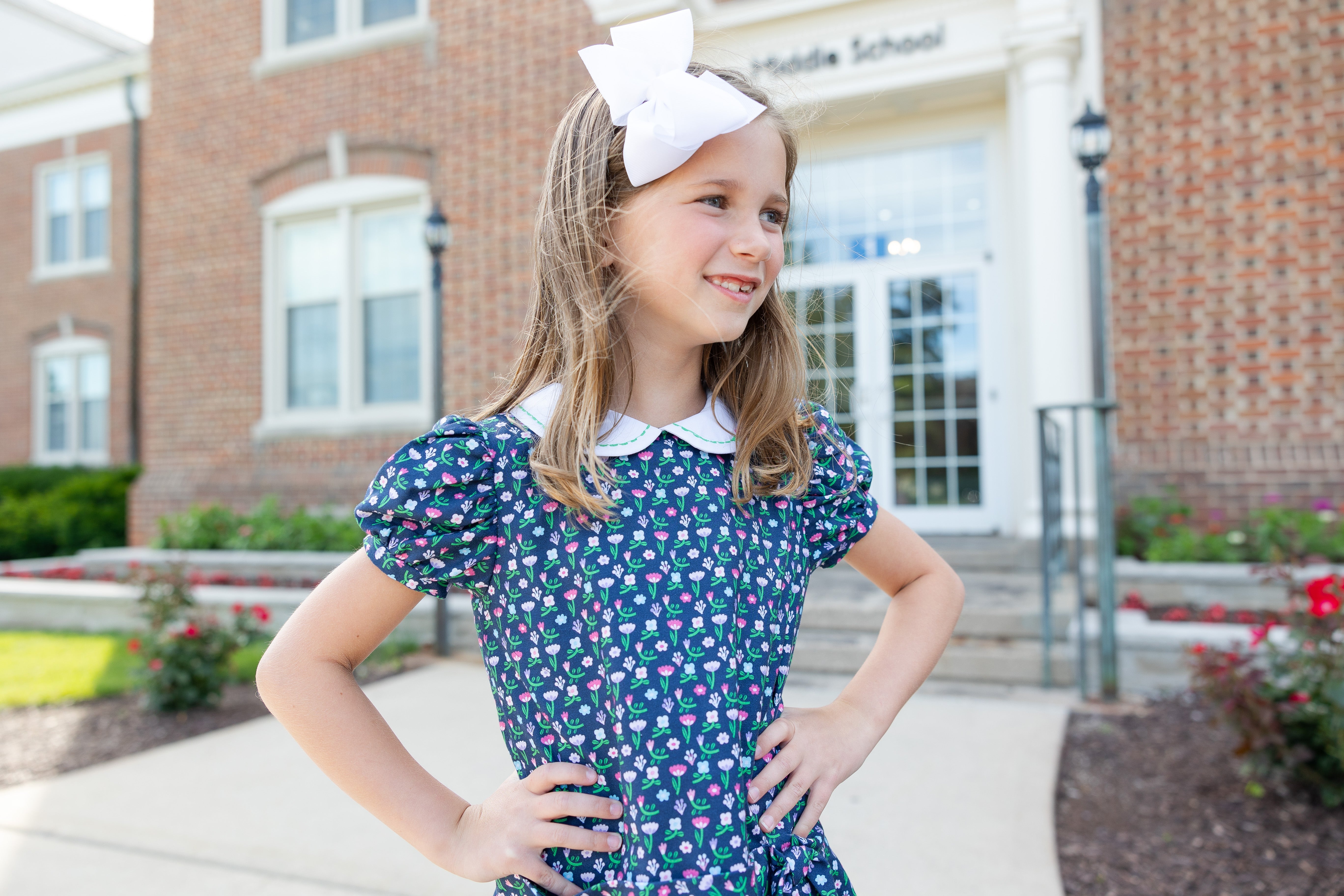 girl in floral dress and white hairbow outside of a brick building