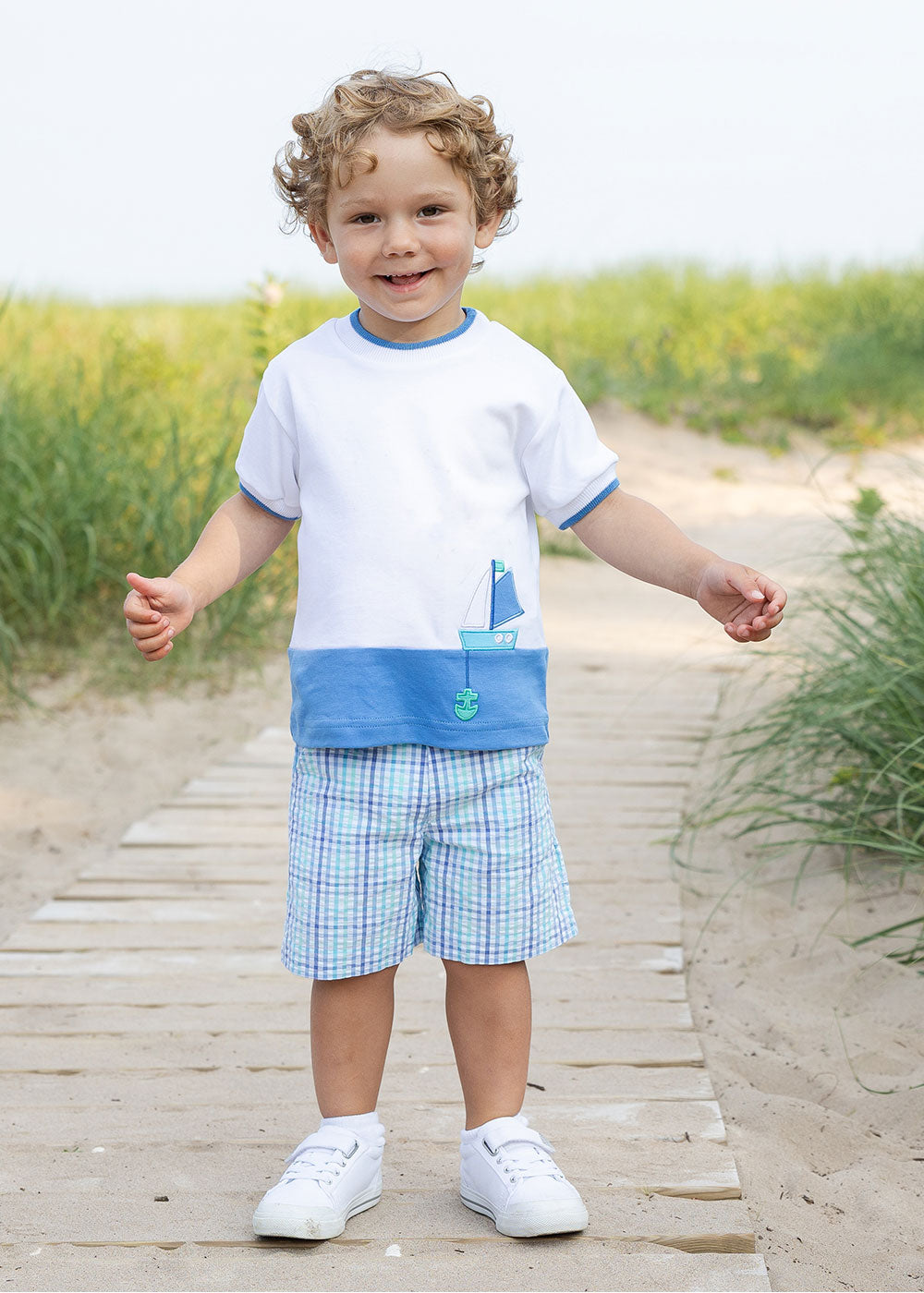 young boy in knit shirt with sailboat on boardwalk