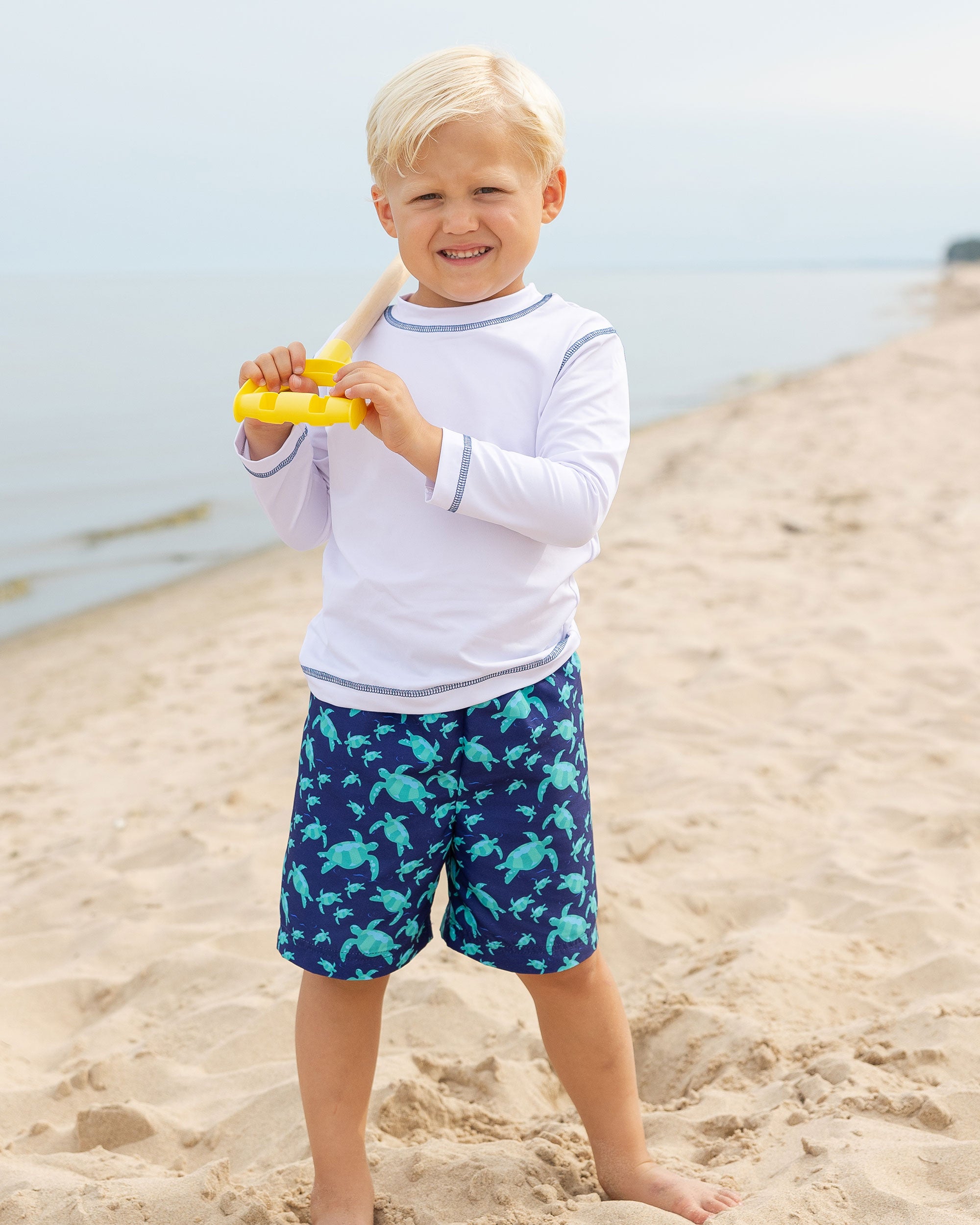 boy on beach in navy swim trunk with sea turtles