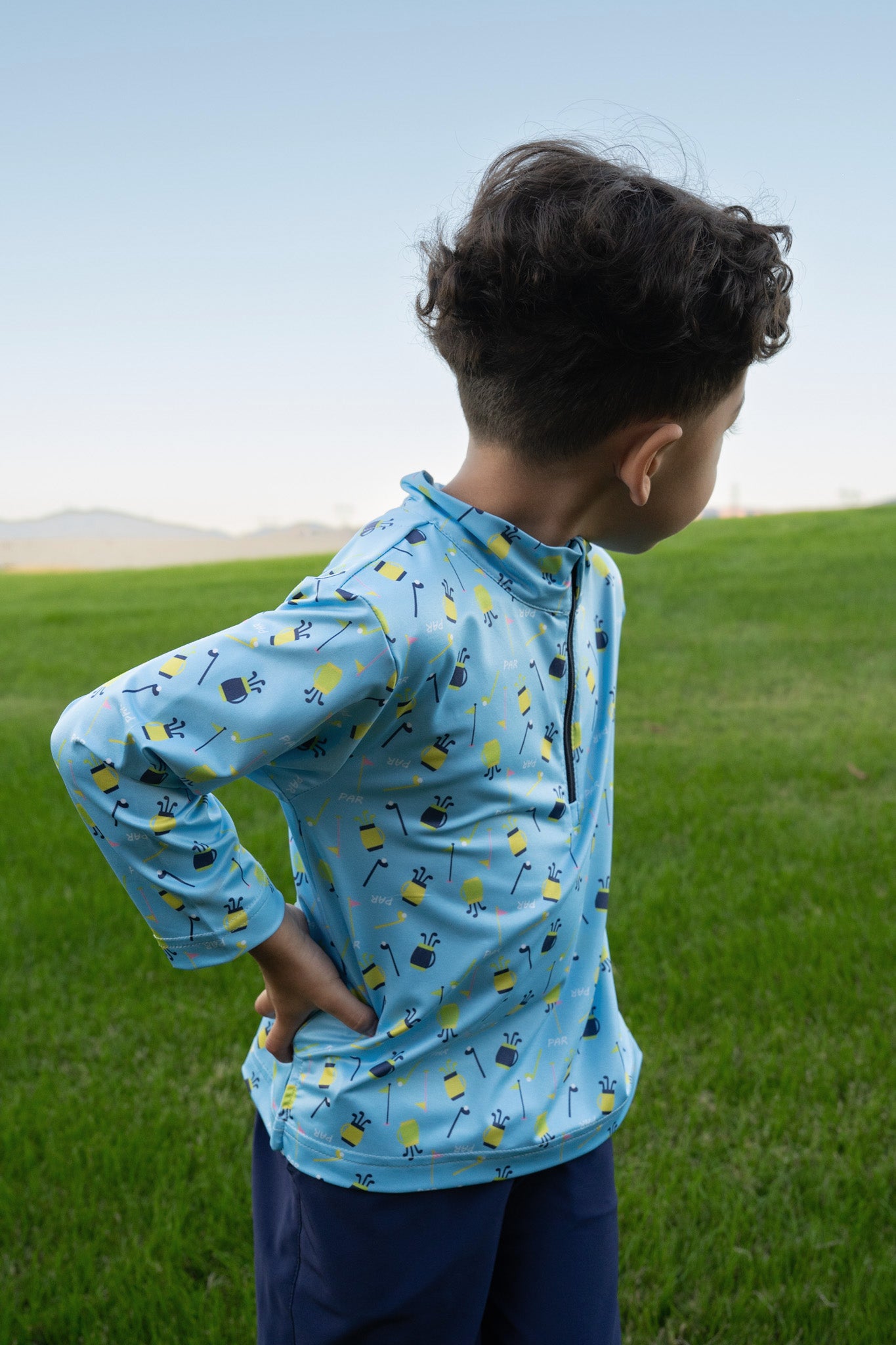 Child wearing a blue jacket with a pattern standing in a grassy field.