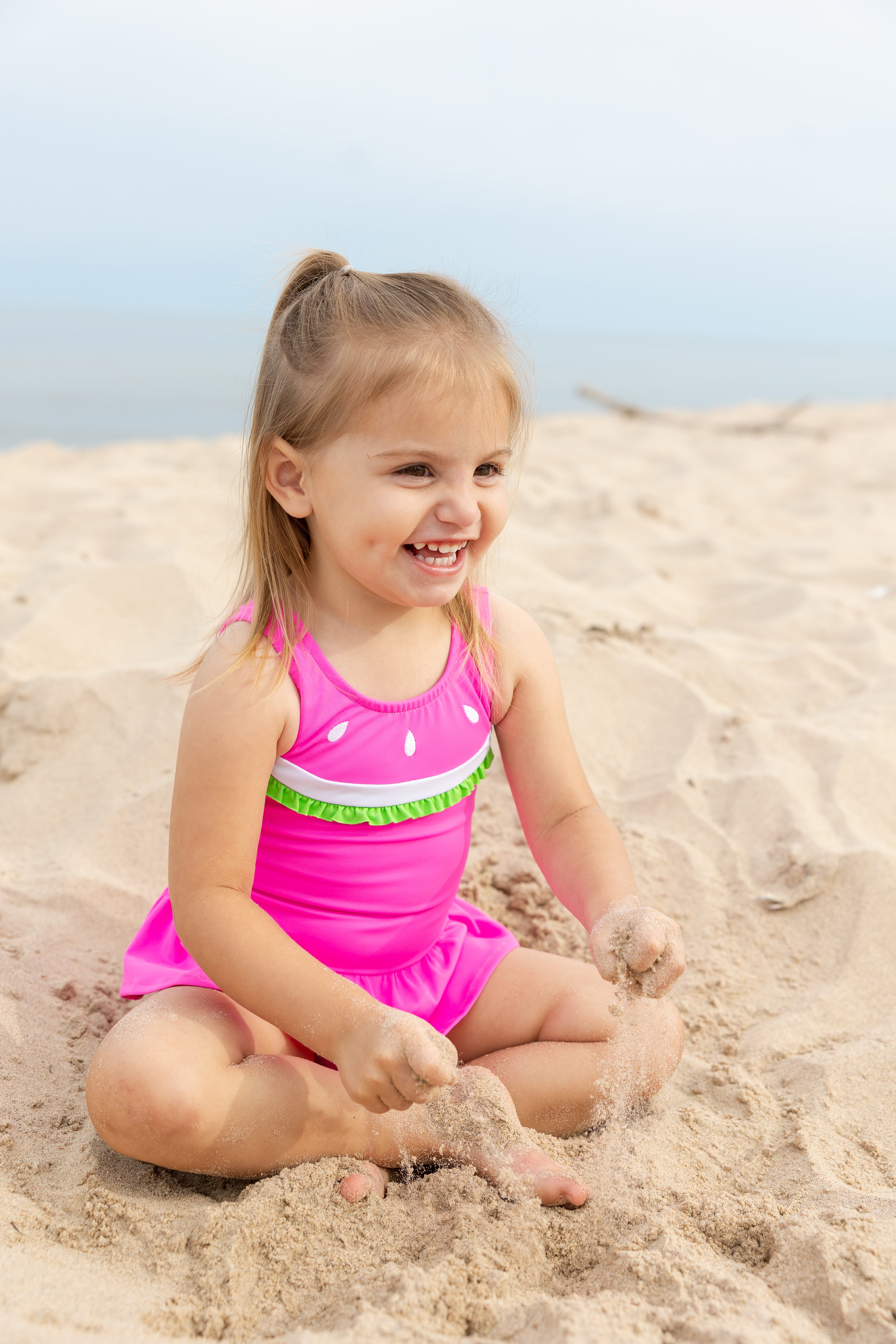 young girl on beach smiling in watermelon swimsuit