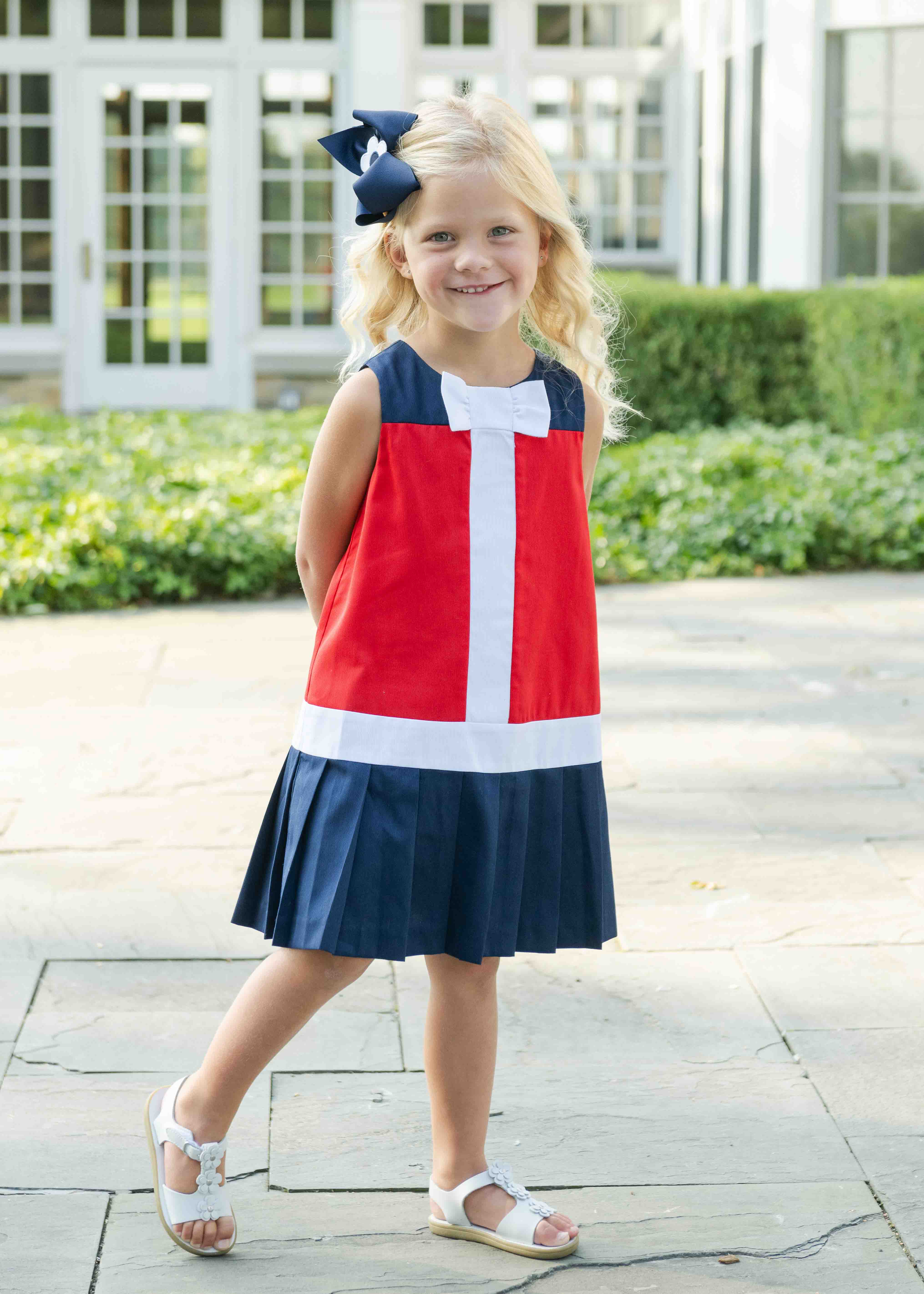 young girl in red and navy dress with white bow outside