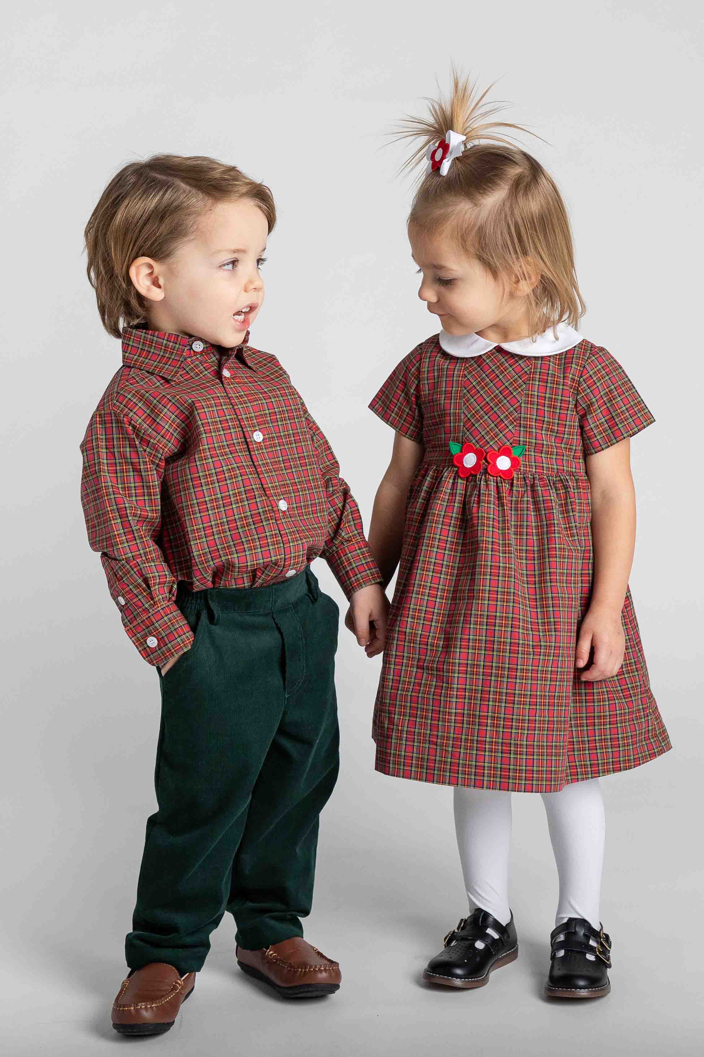 Two children in matching plaid outfits standing against a plain background