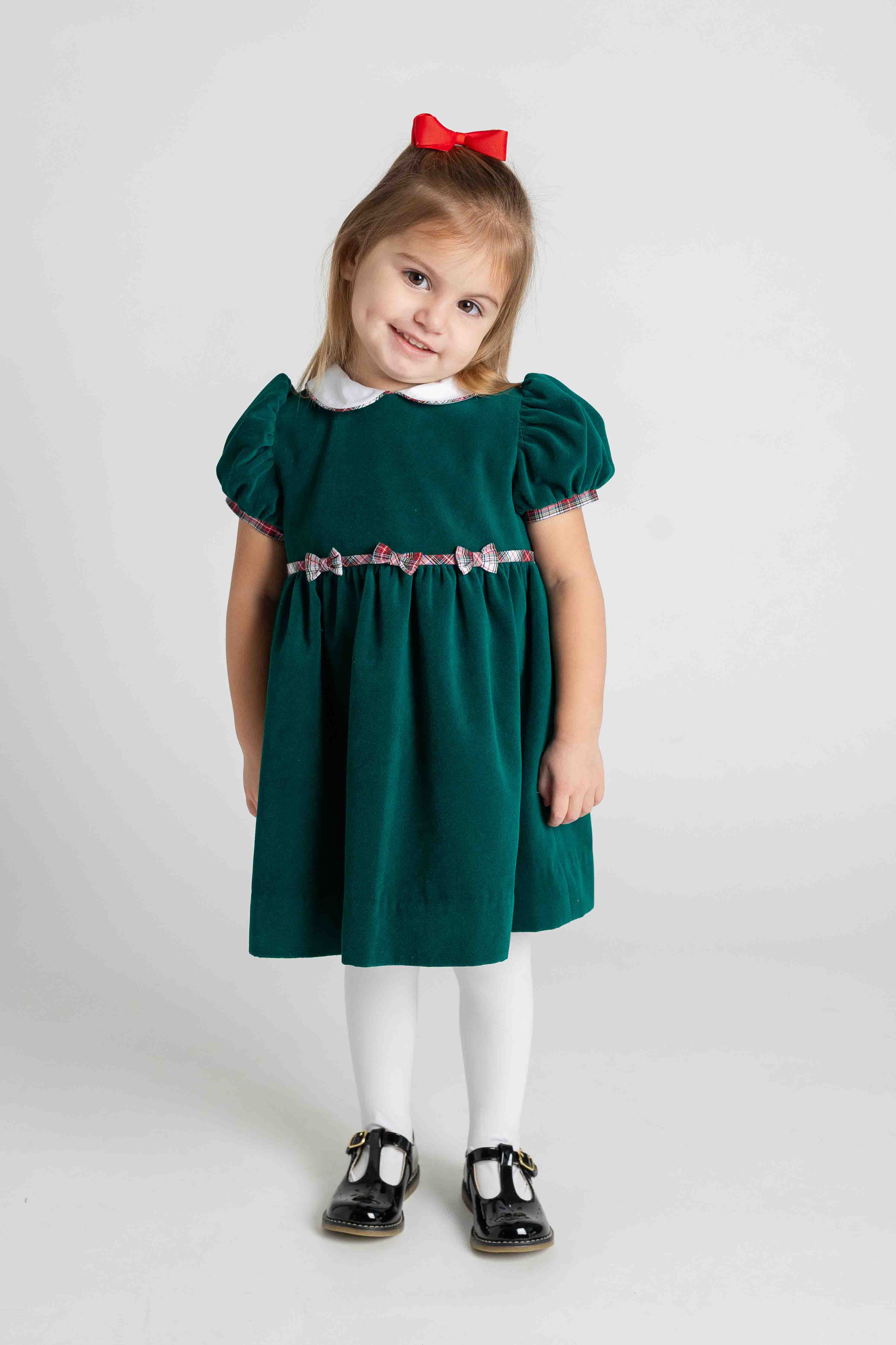 Young girl wearing a green dress with a white collar and red bow on a white background