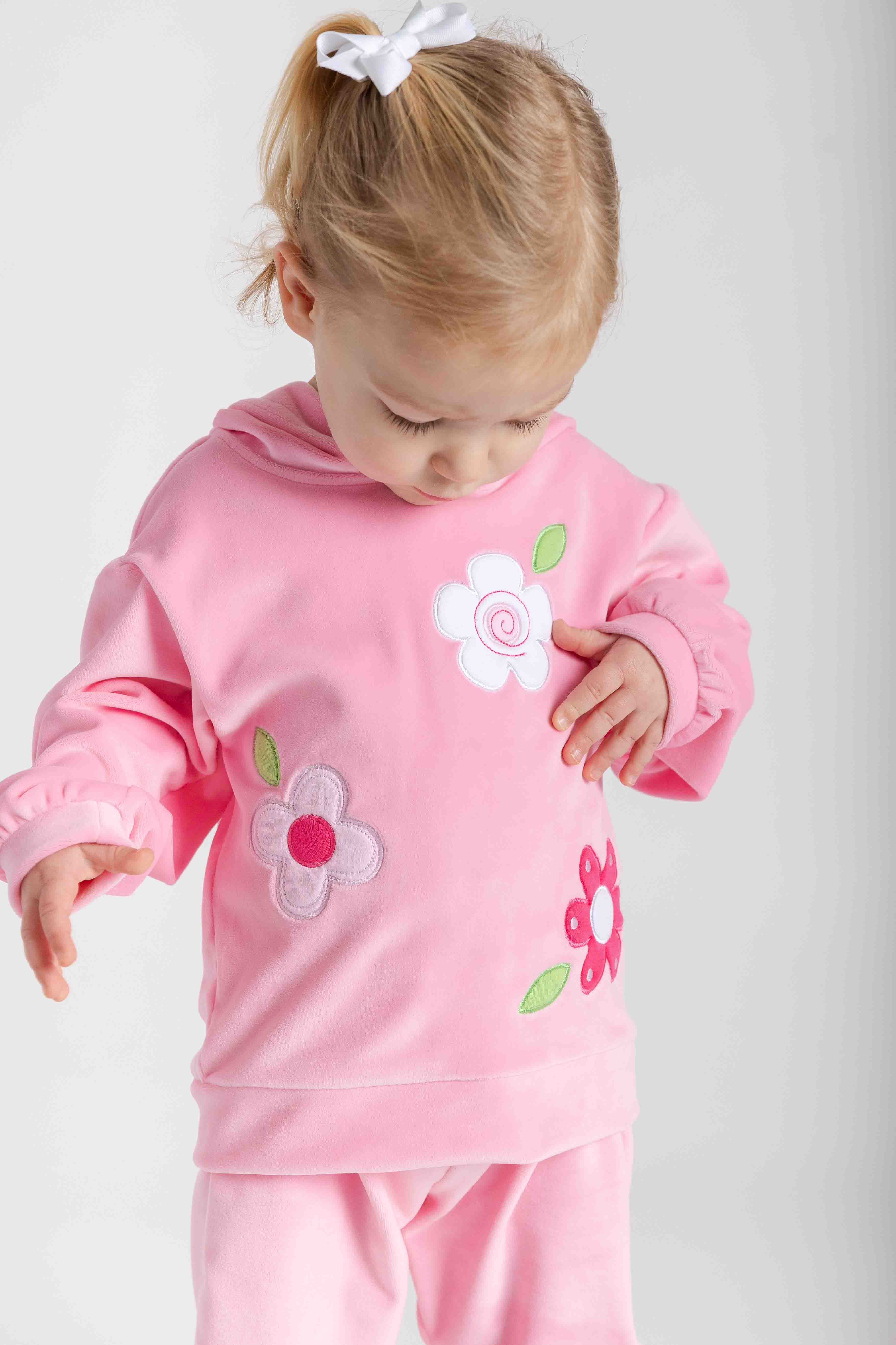 Child wearing a pink outfit with flower designs on a plain background
