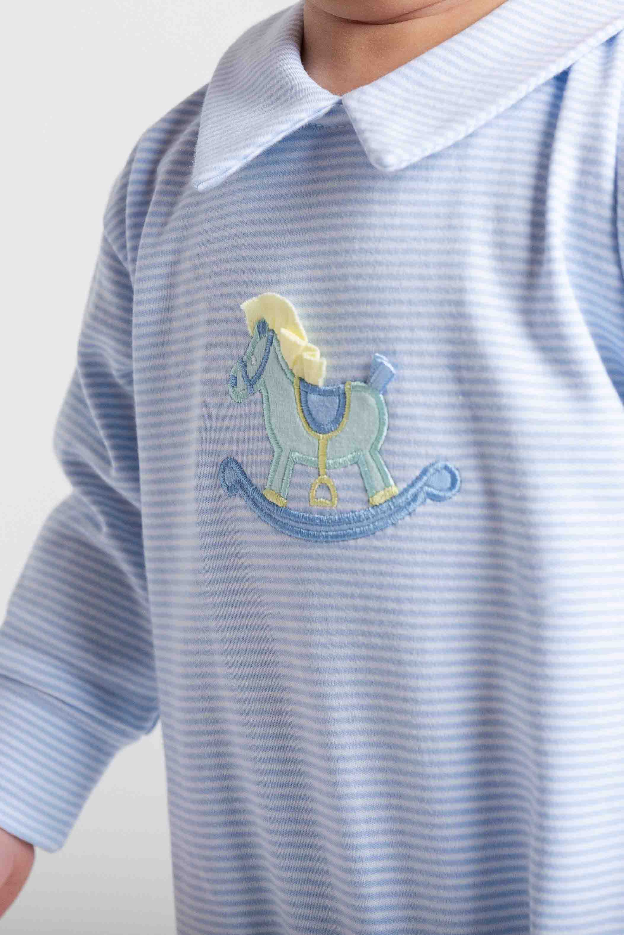 Close-up of a baby's outfit with a striped longall and embroidered rocking horse design.