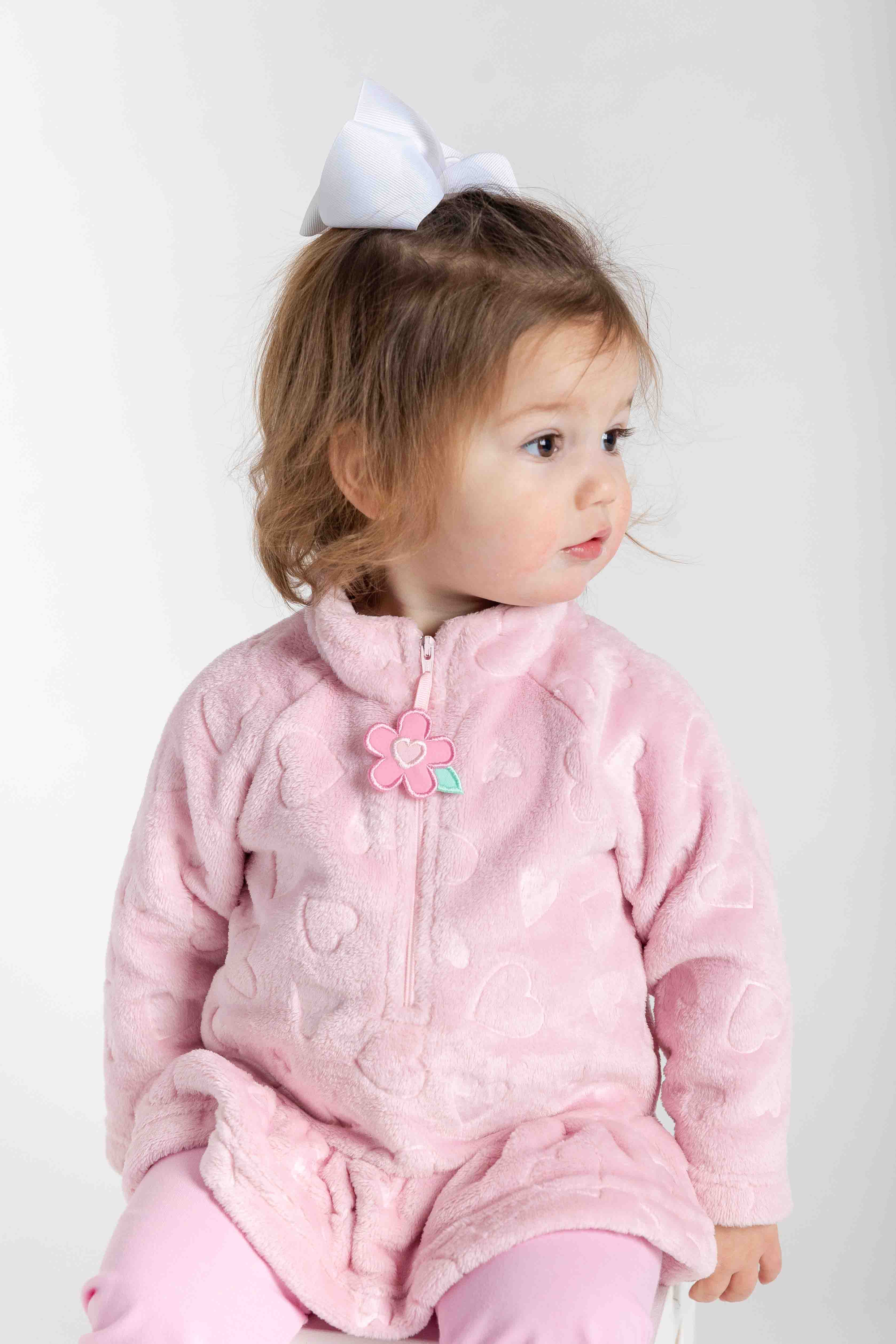 Child wearing a pink outfit with a flower detail on a white background