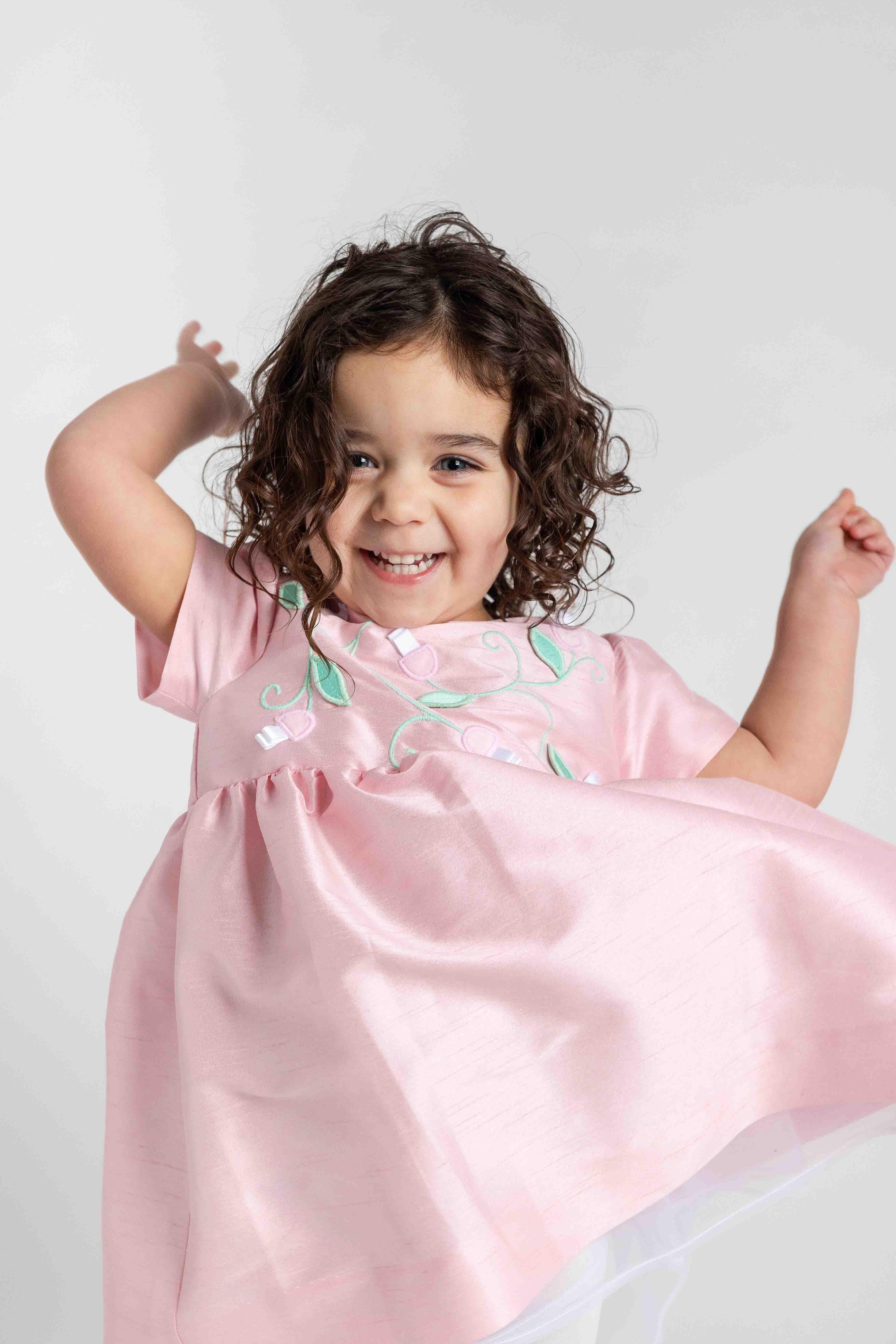 Child wearing a pink dress with floral details on a white background