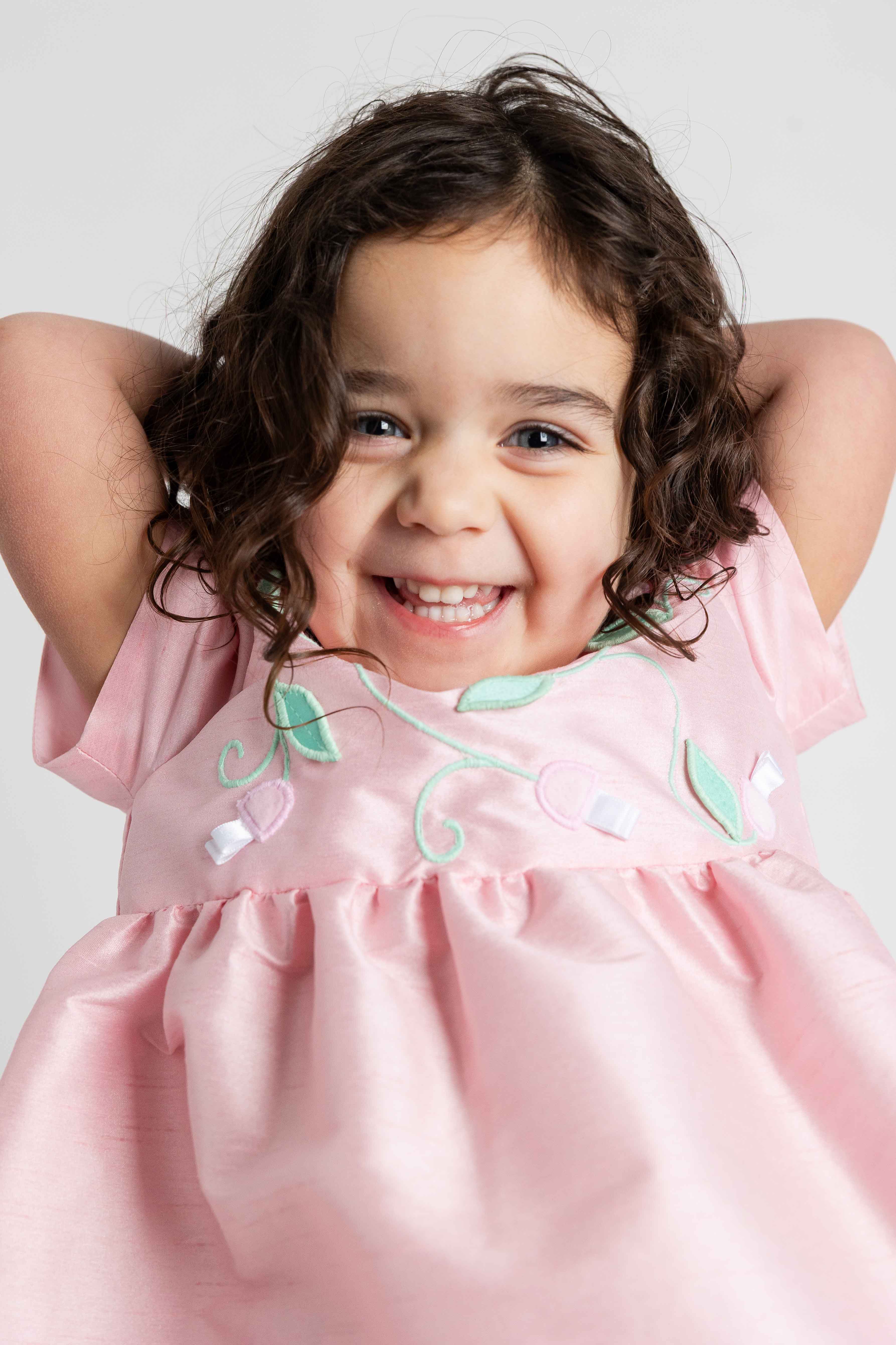 Child wearing a pink dress with green accents against a plain background