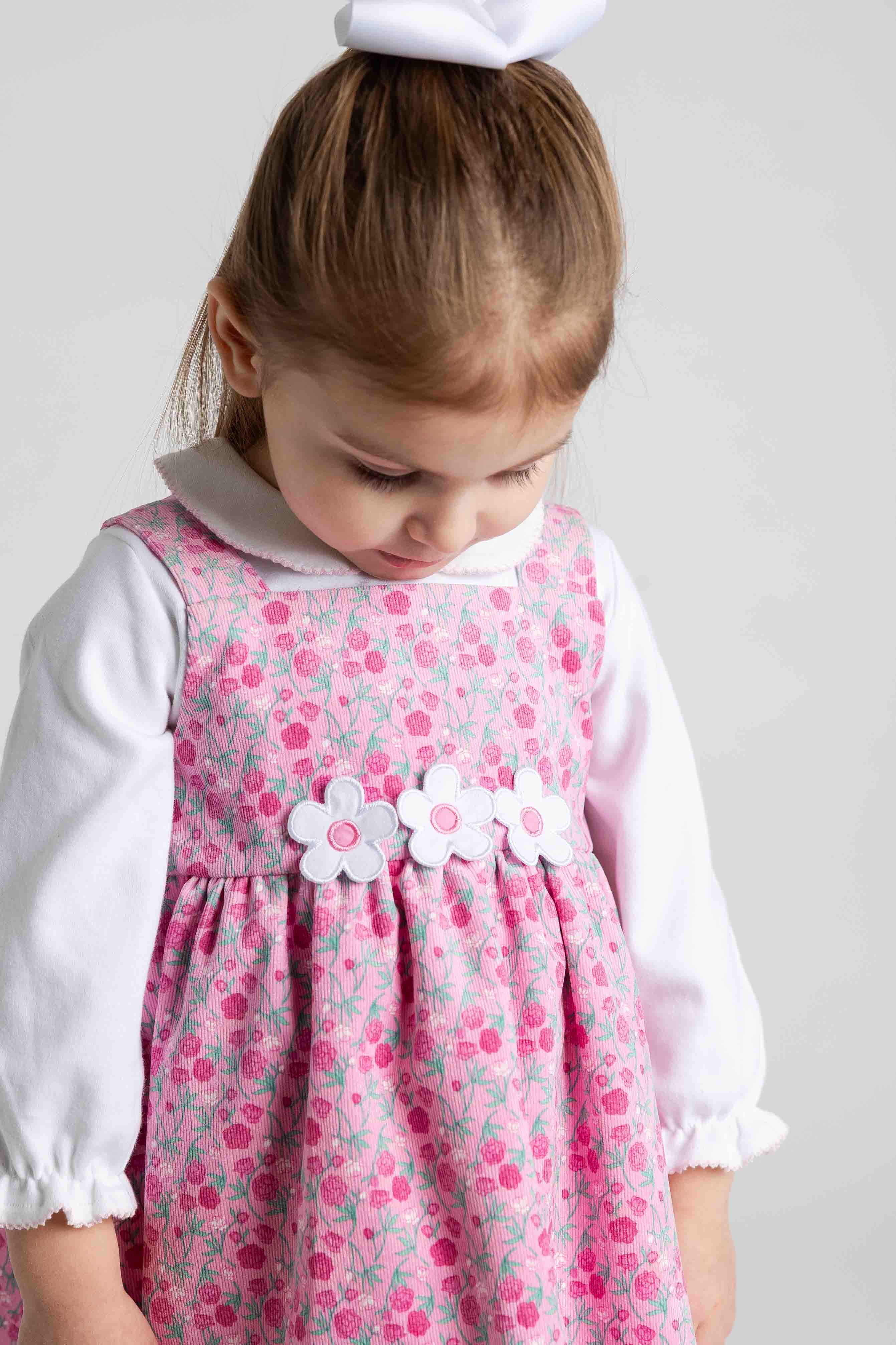 Young girl wearing a pink floral dress with white flowers and a white collar against a plain background