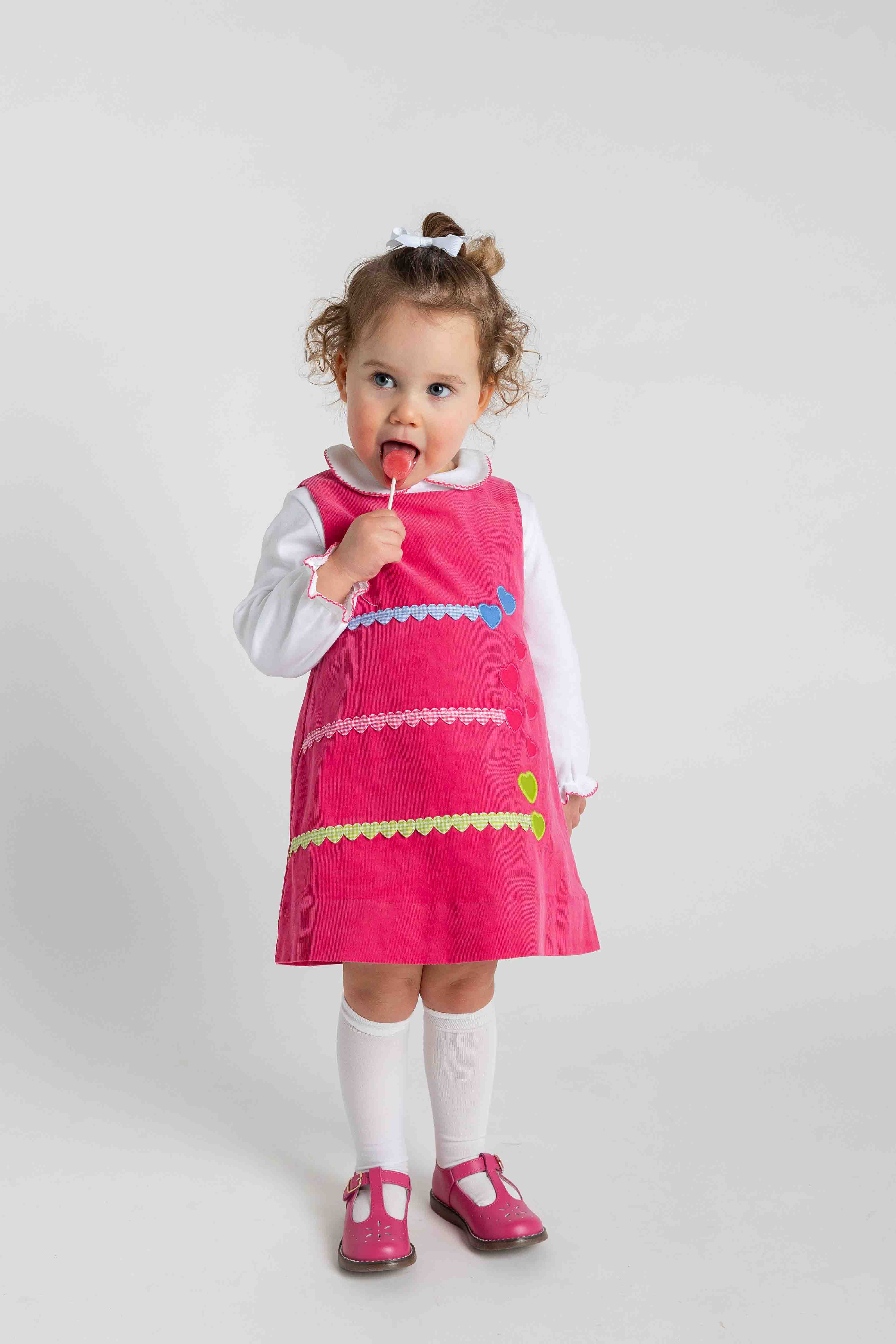 Child wearing a pink dress with colorful accents on a white background