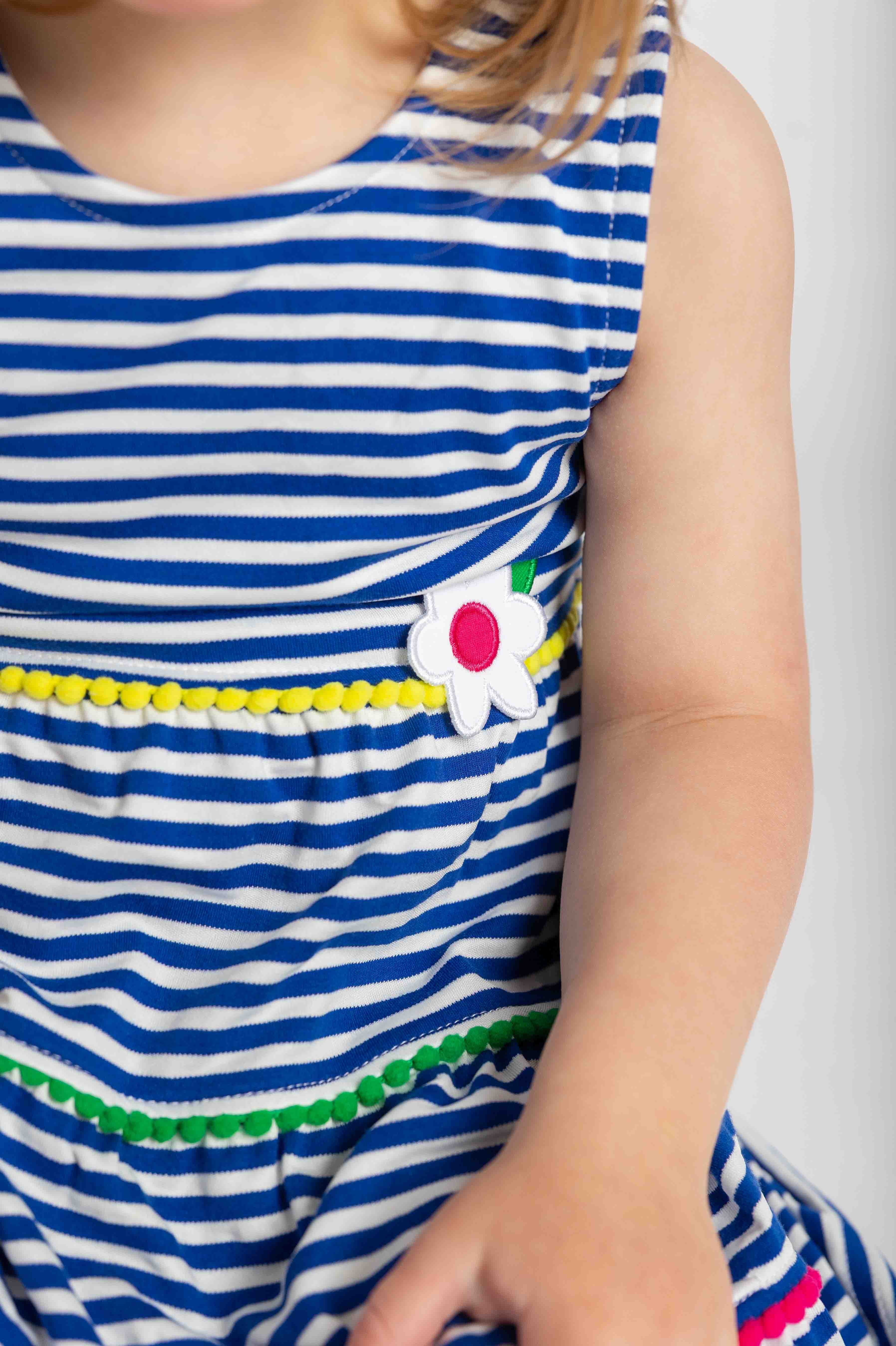 Close-up of a child wearing a blue and white striped dress with a flower detail on a plain background