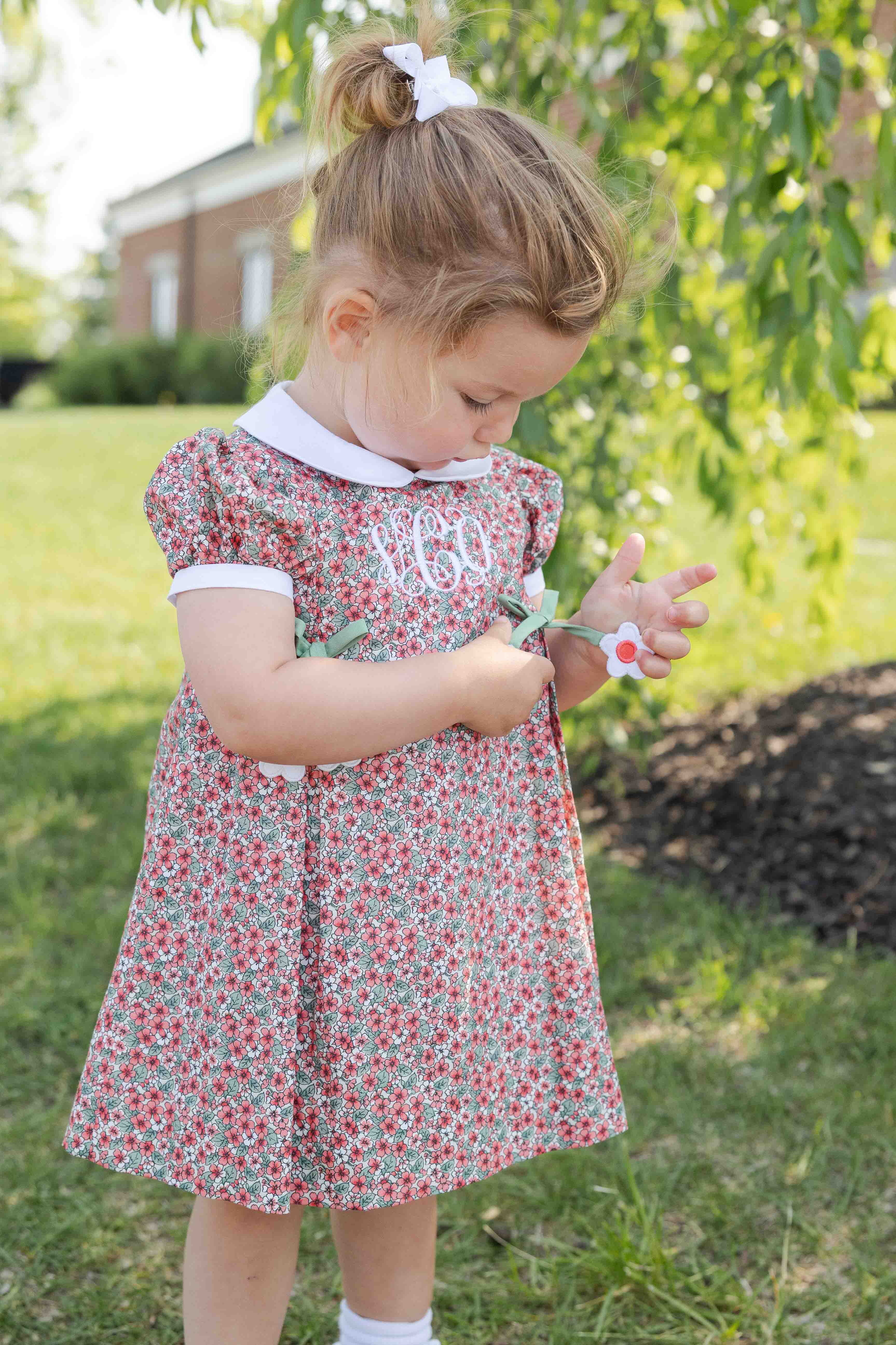 Young girl in a floral dress standing outdoors with greenery in the background