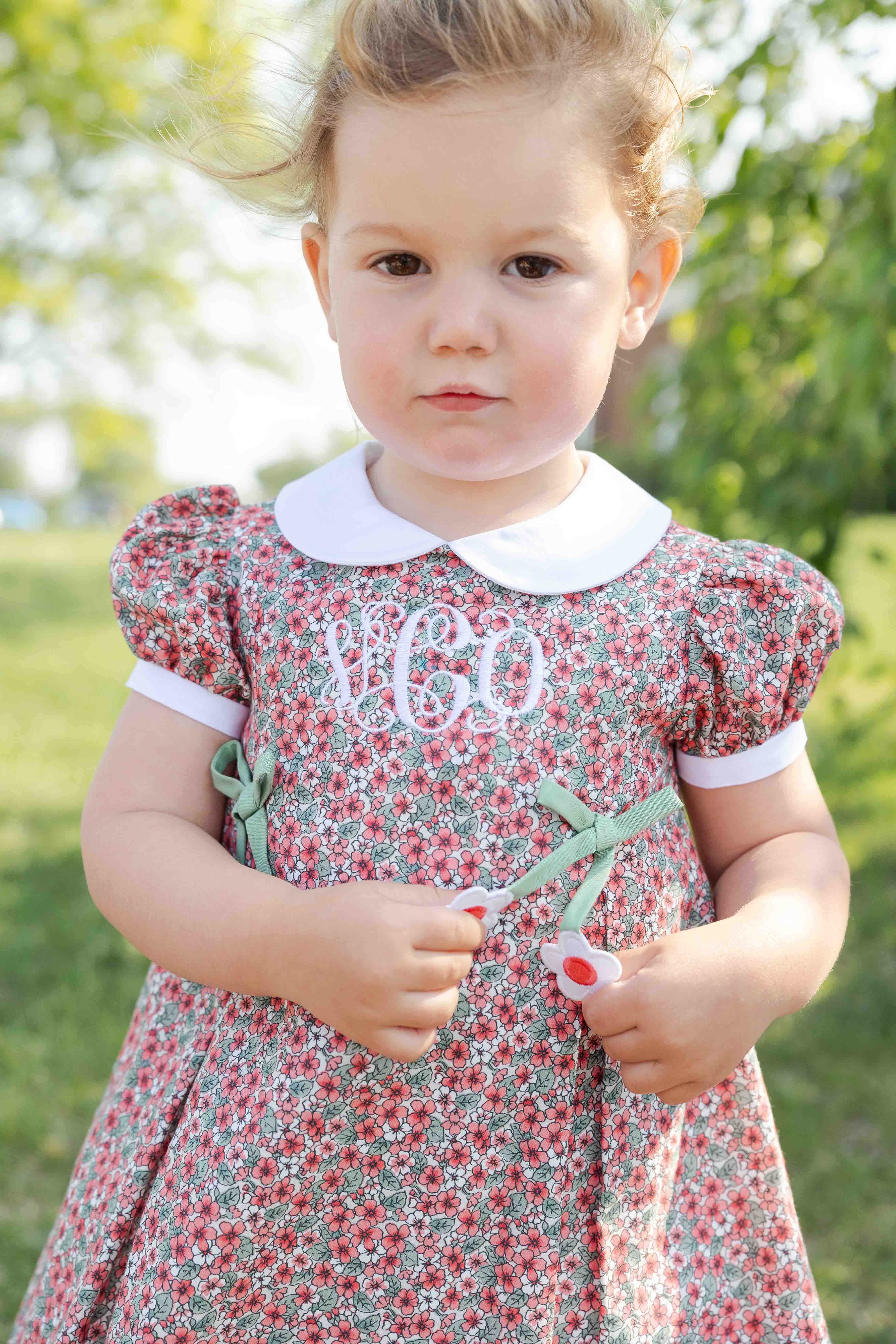 Young girl wearing a floral dress with a monogram in an outdoor setting