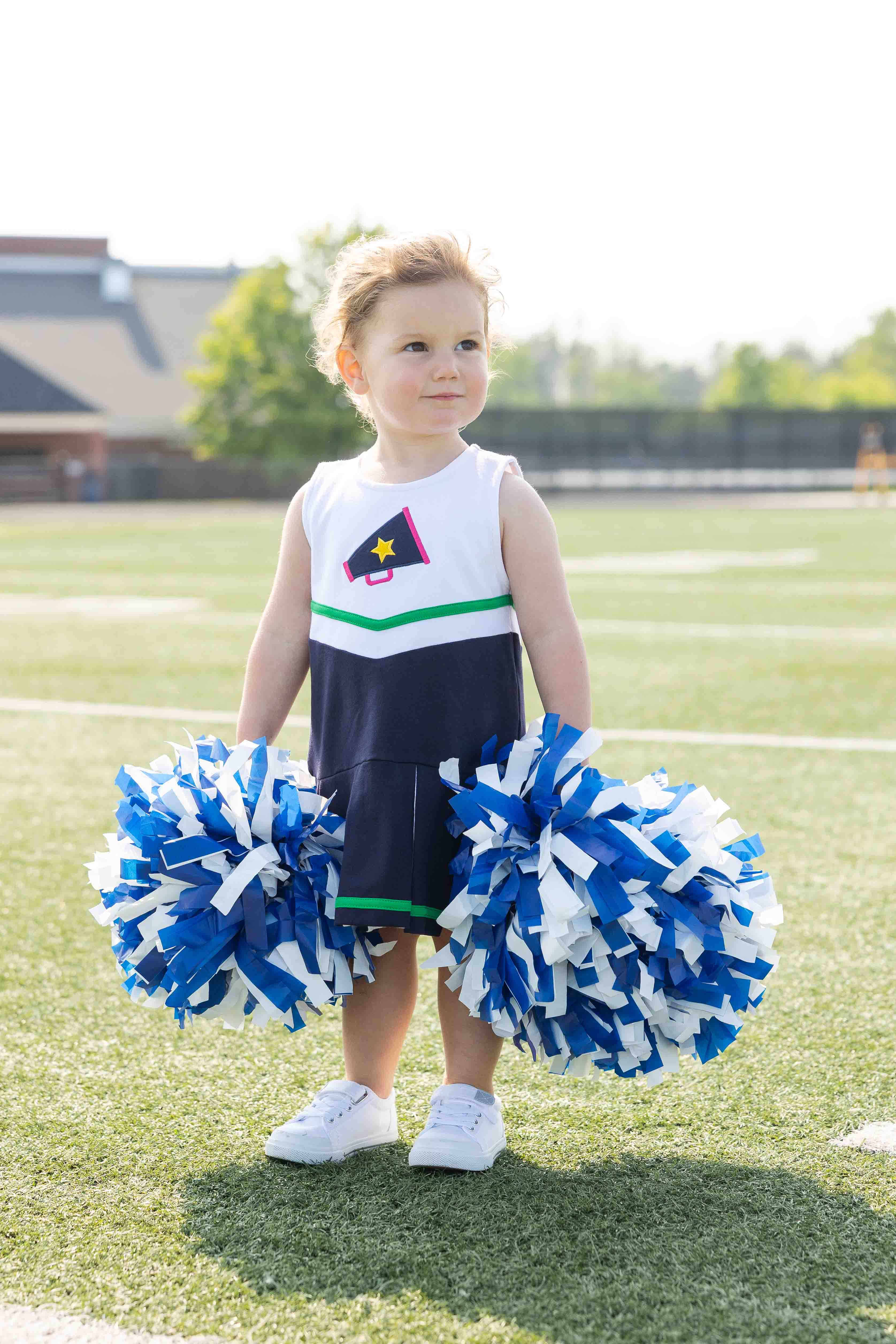 Child in a cheerleading outfit with pom-poms on a sports field