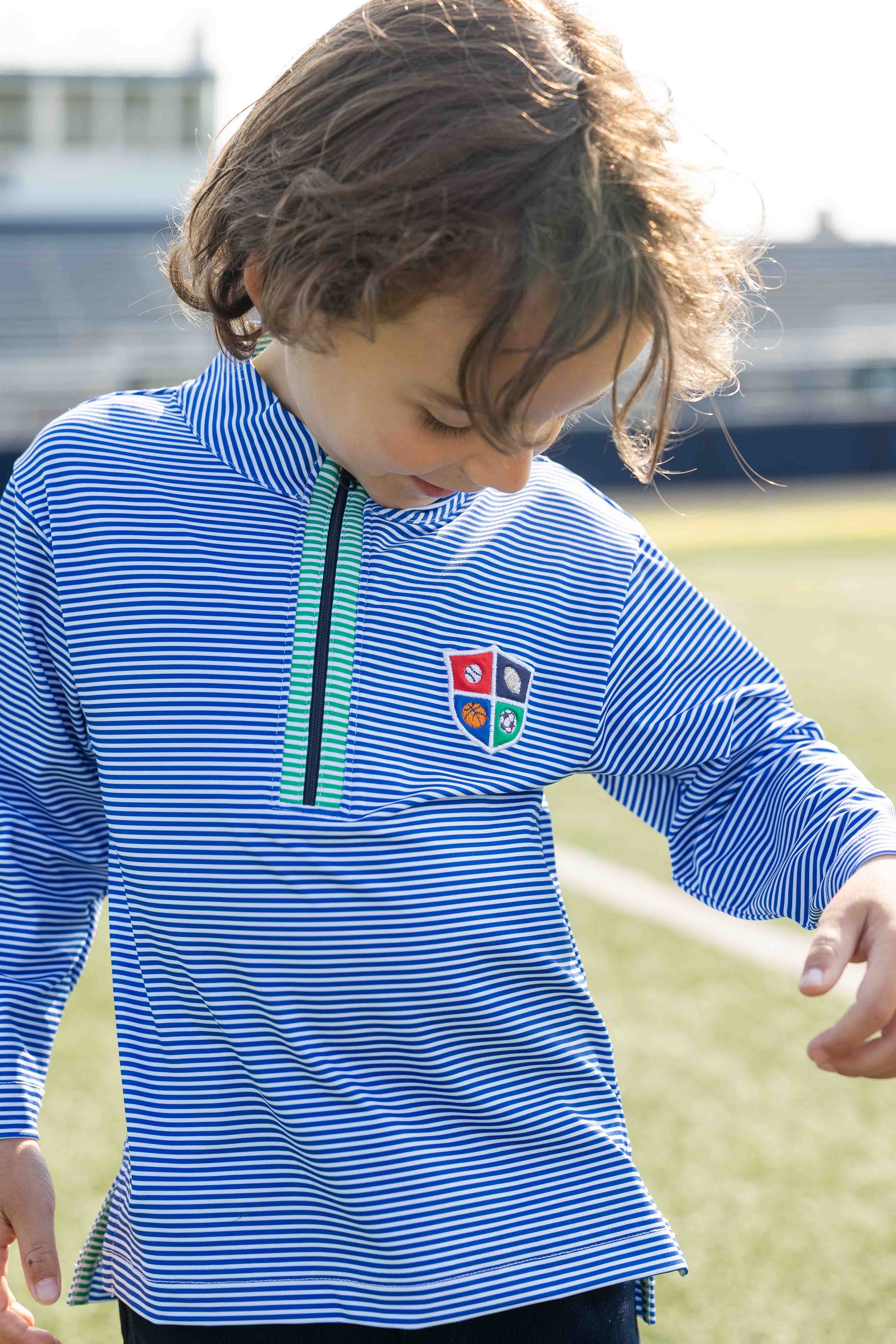Child wearing a blue striped shirt with a logo on a grassy field