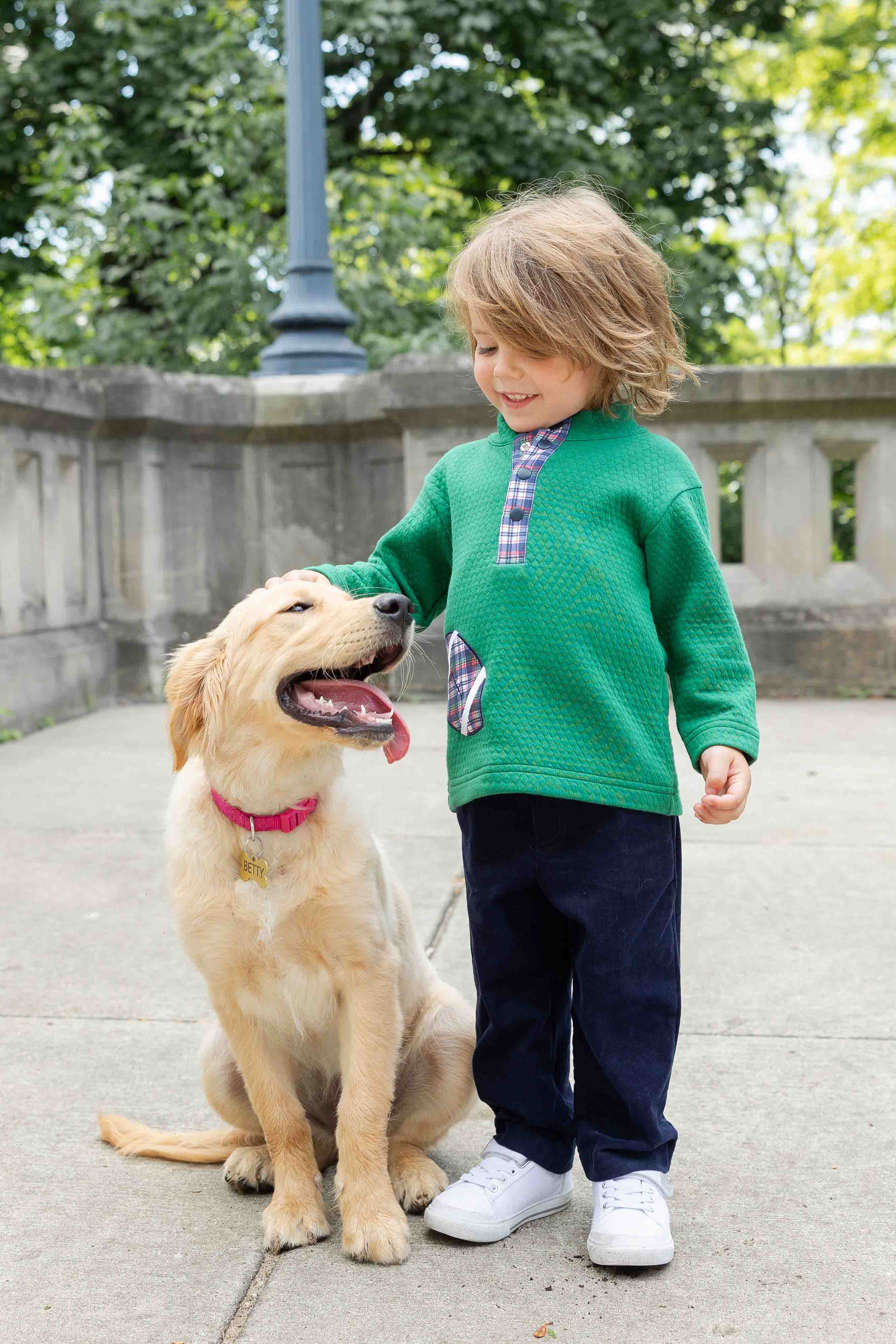 Child in a green sweater standing next to a dog outdoors