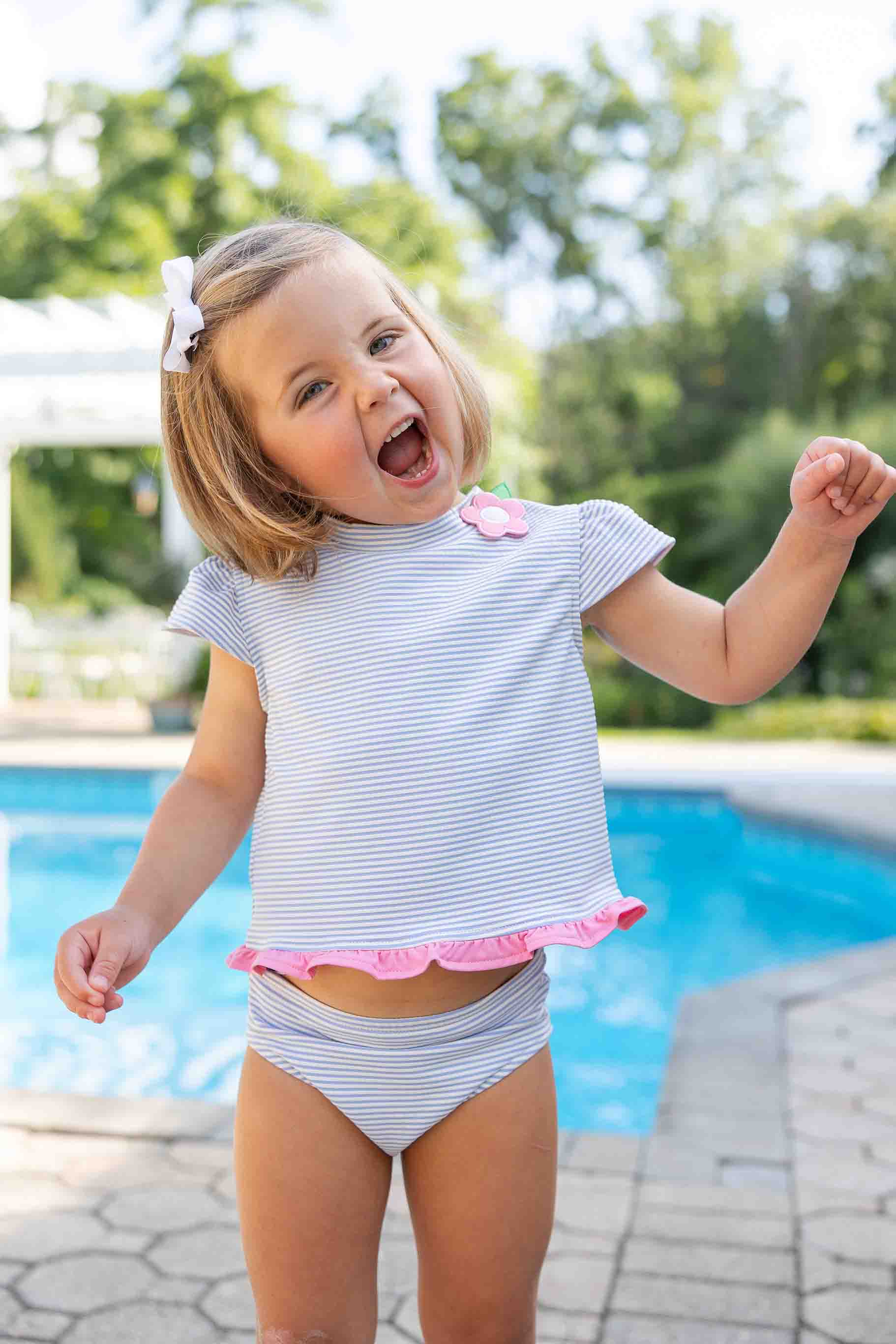 Child in a striped swimsuit with ruffled bottom standing by a pool