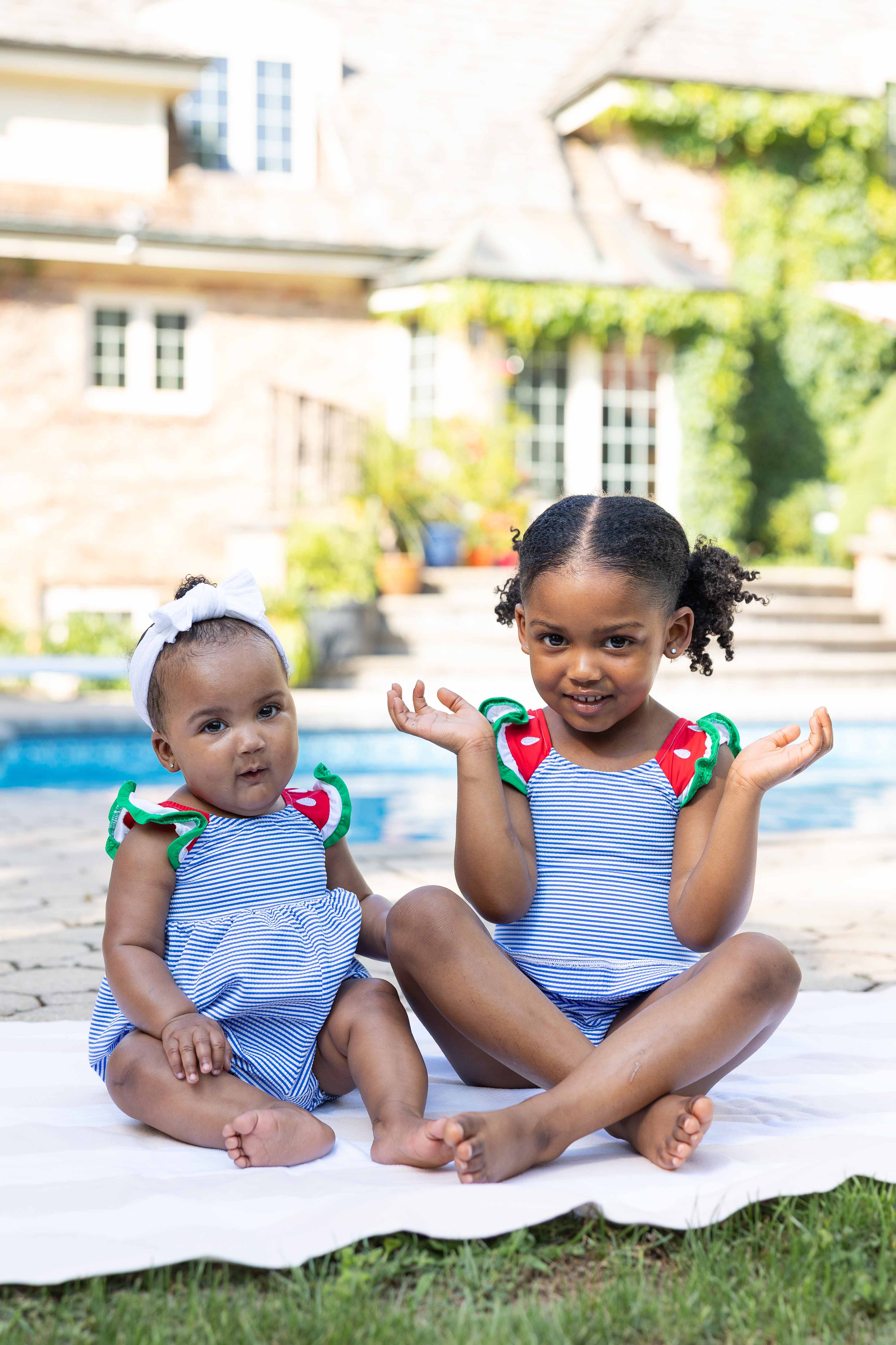 Two young girls in matching blue swimsuits with red and green accents sitting by a pool.