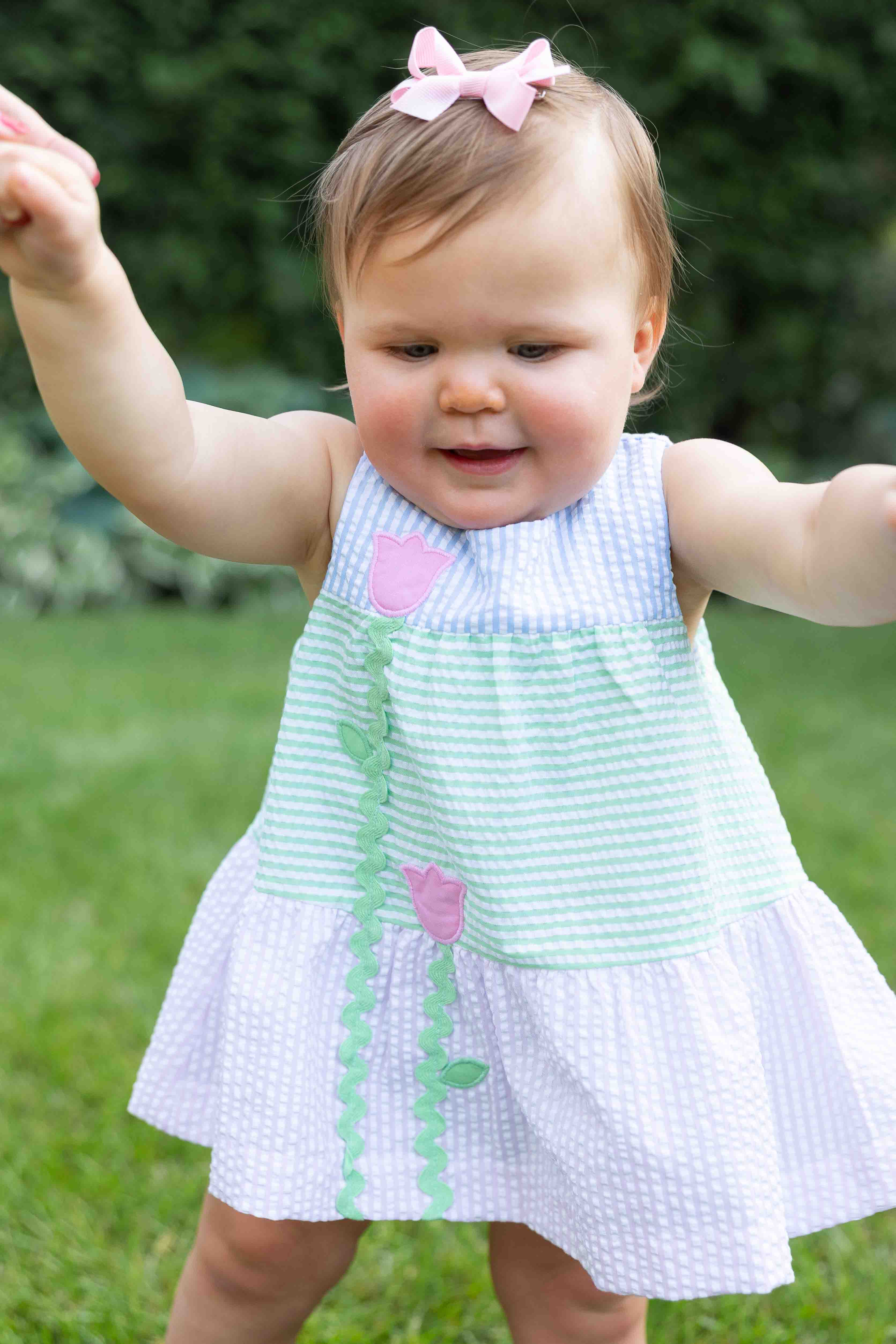 Child wearing a light blue dress with pink flowers and green trim outdoors.