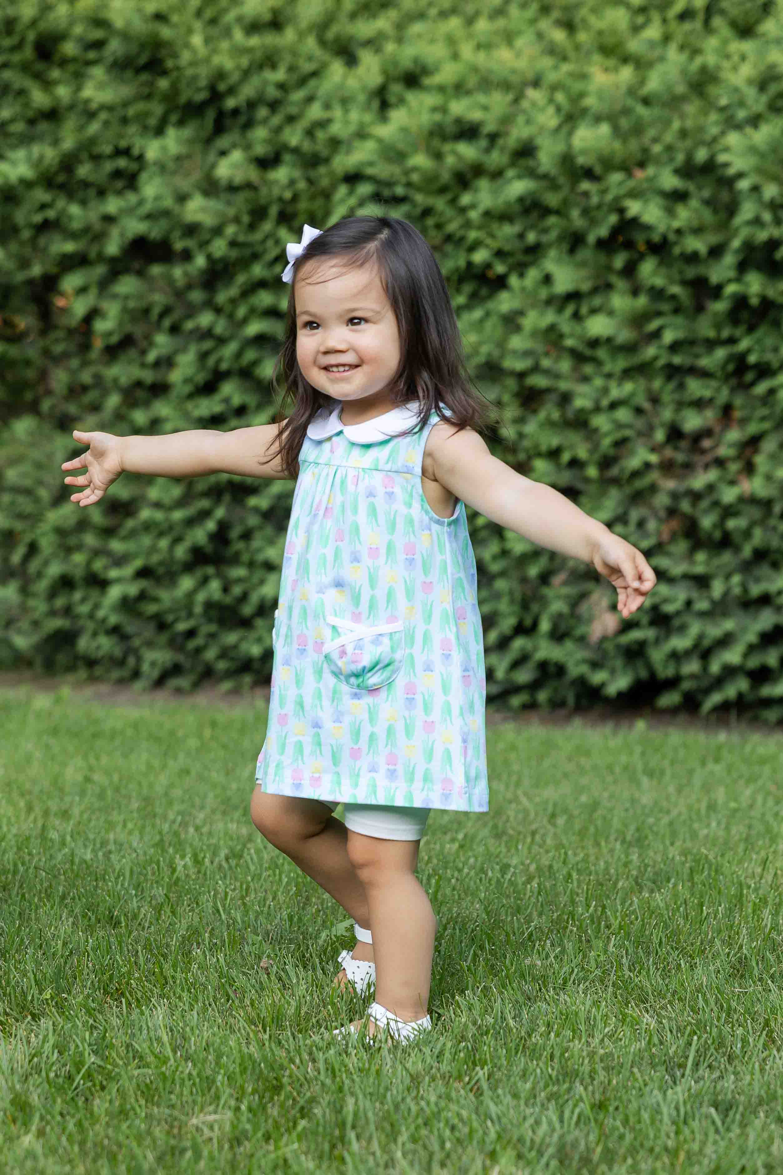 Child in a colorful dress standing on grass with green bushes in the background