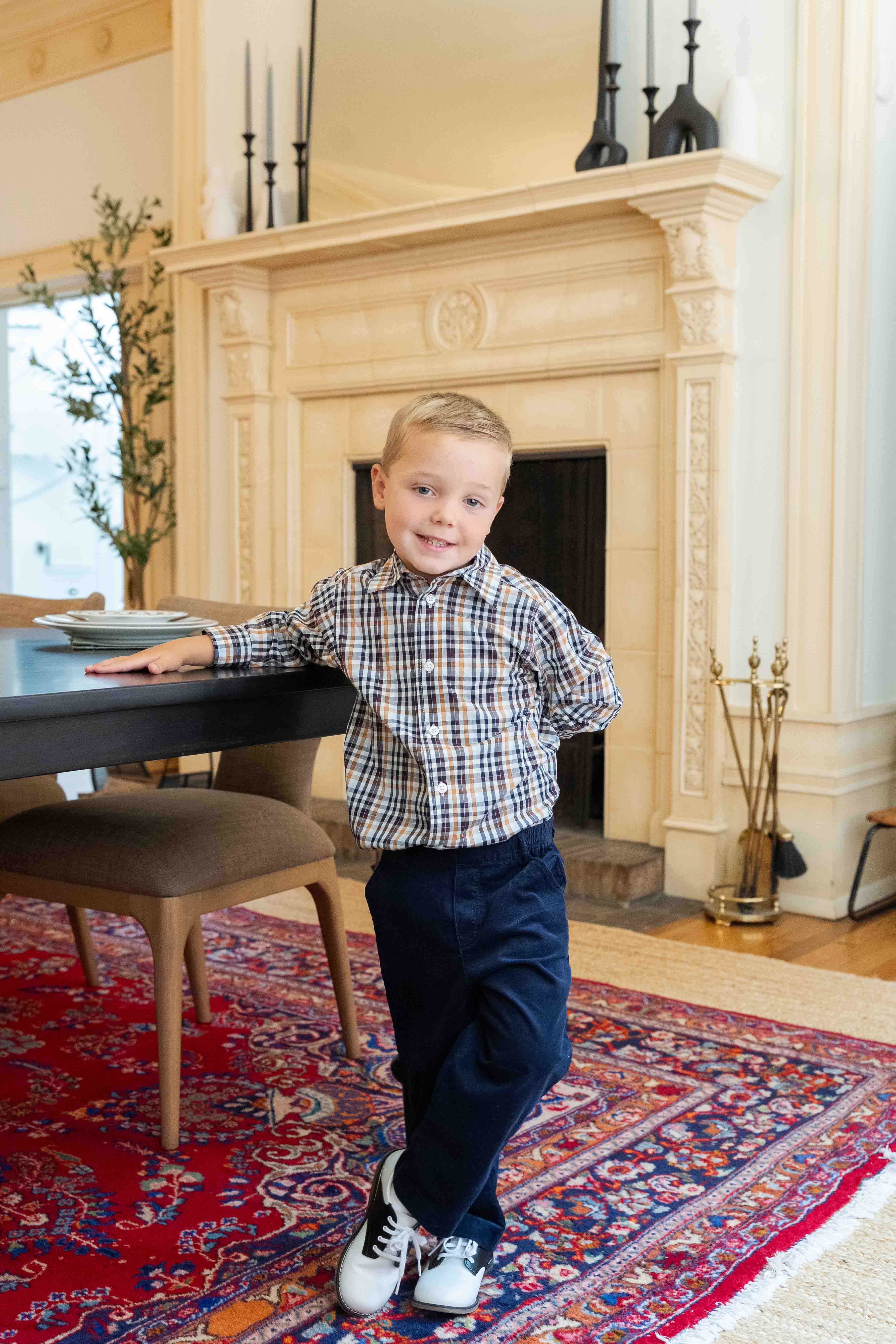 Young boy standing in a room with a fireplace and patterned rug