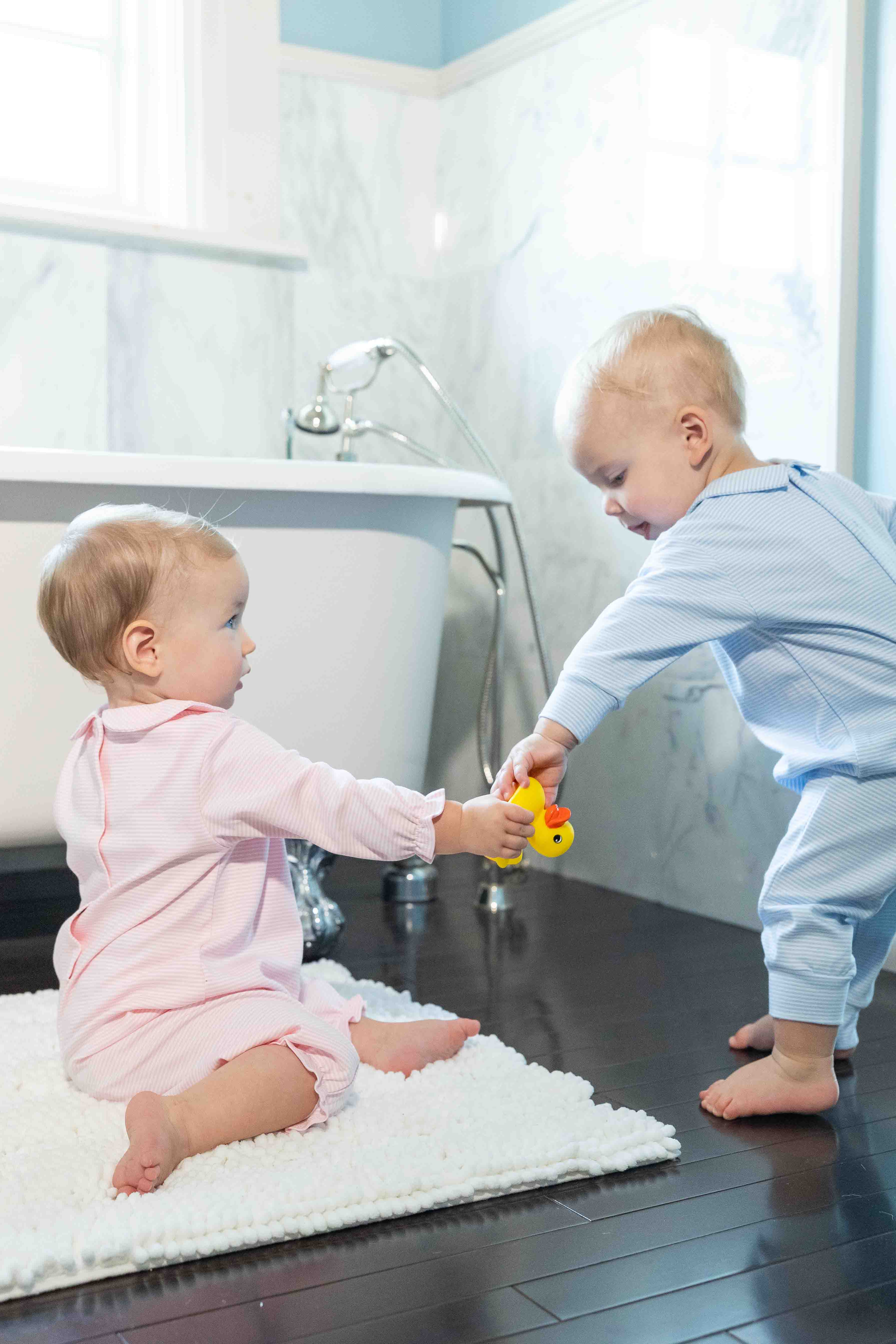 Two children playing with a toy on a wooden bathroom floor.