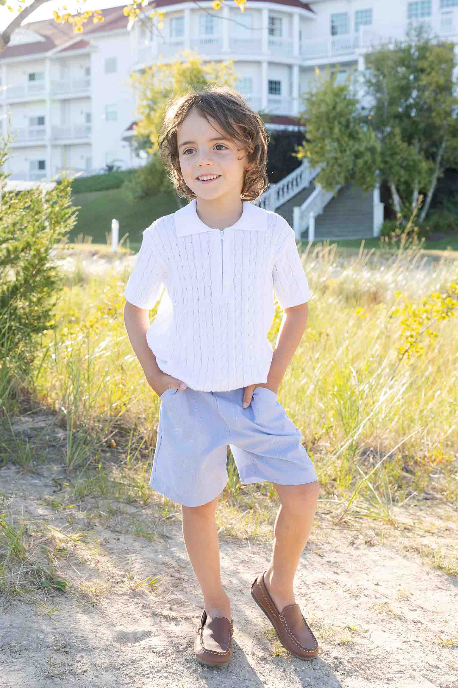 Young boy standing outdoors in a natural setting with buildings in the background