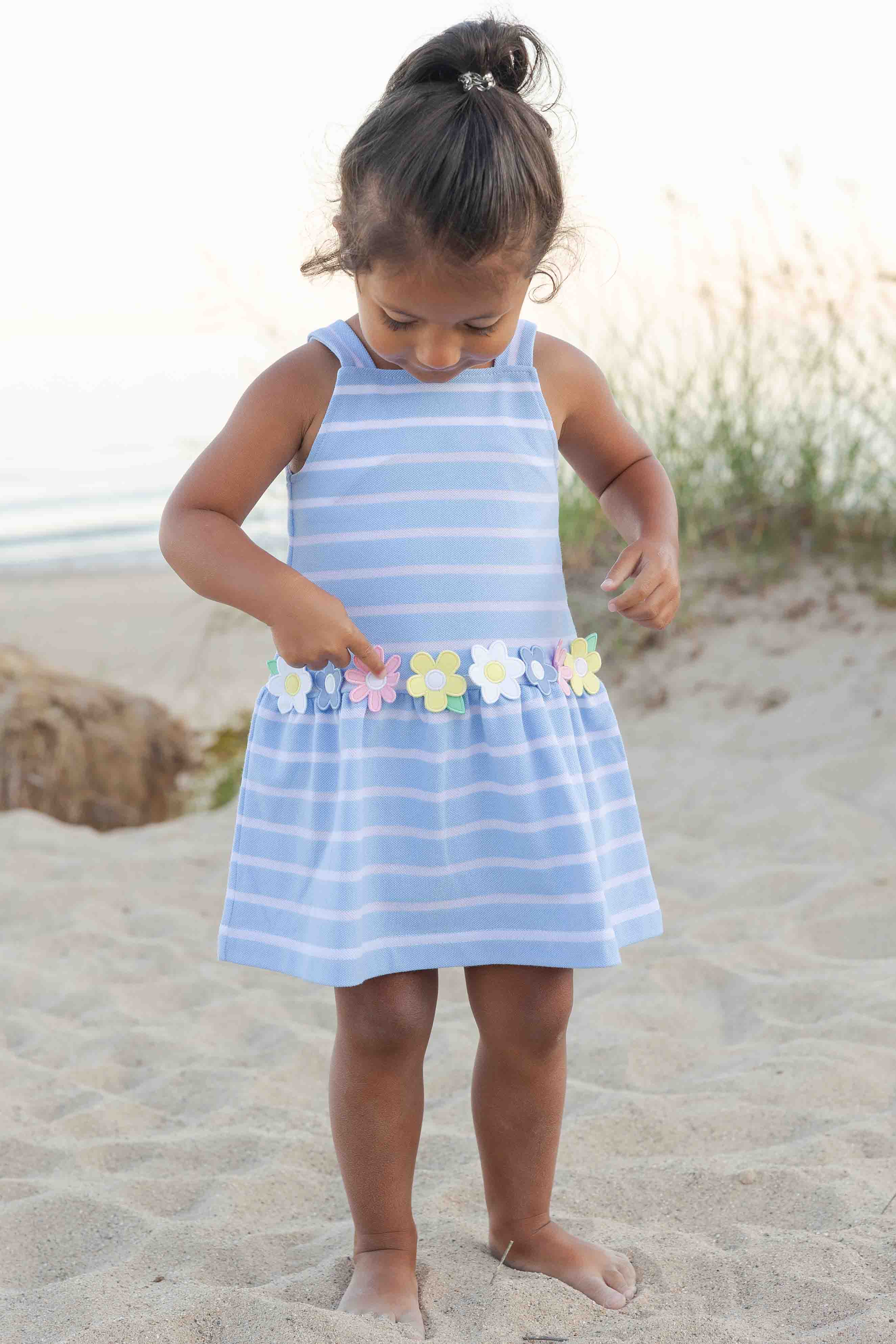 Young girl in a blue striped dress with floral details on a sandy beach.