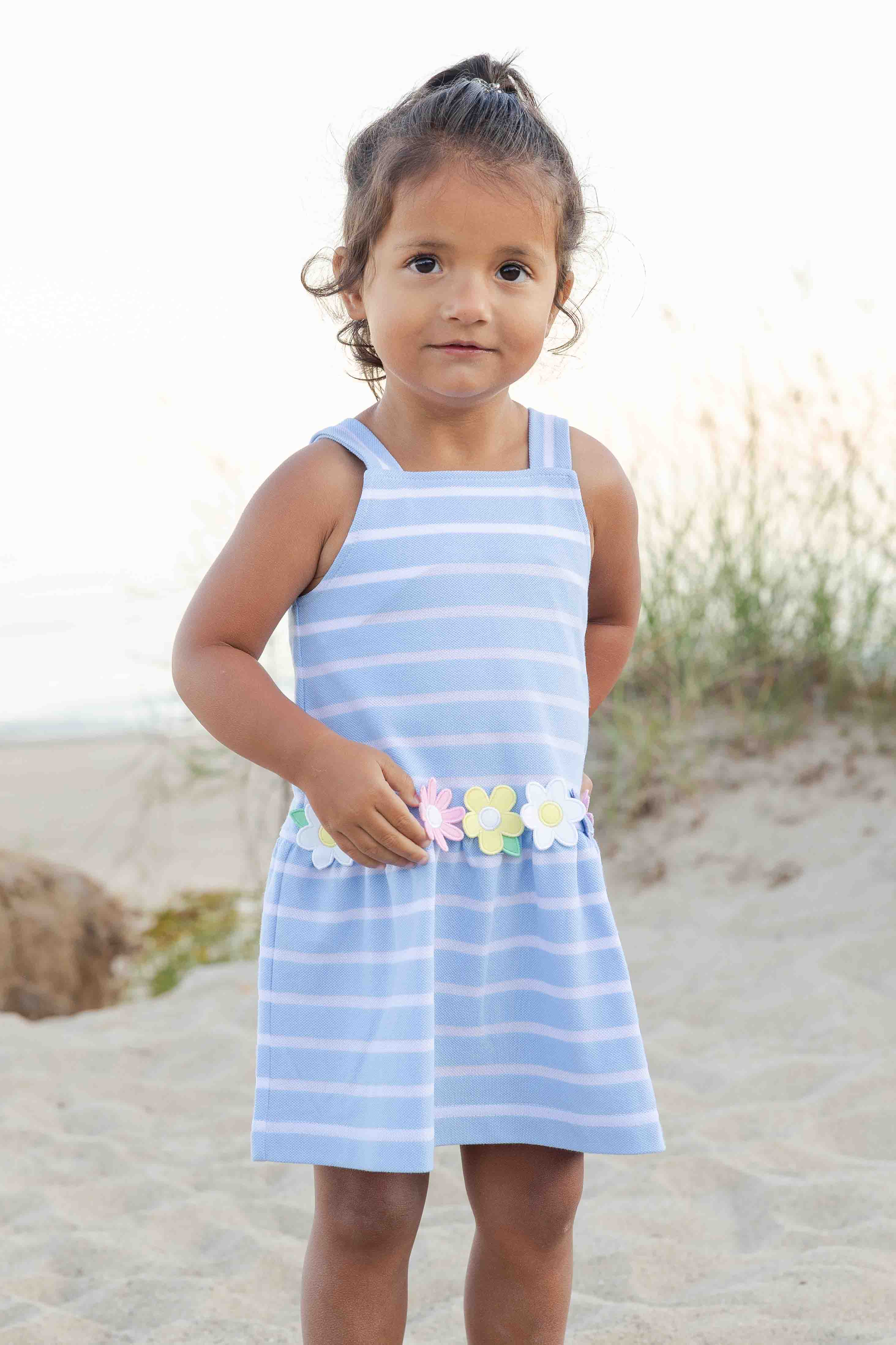 Young girl wearing a blue striped dress with floral details on a beach.