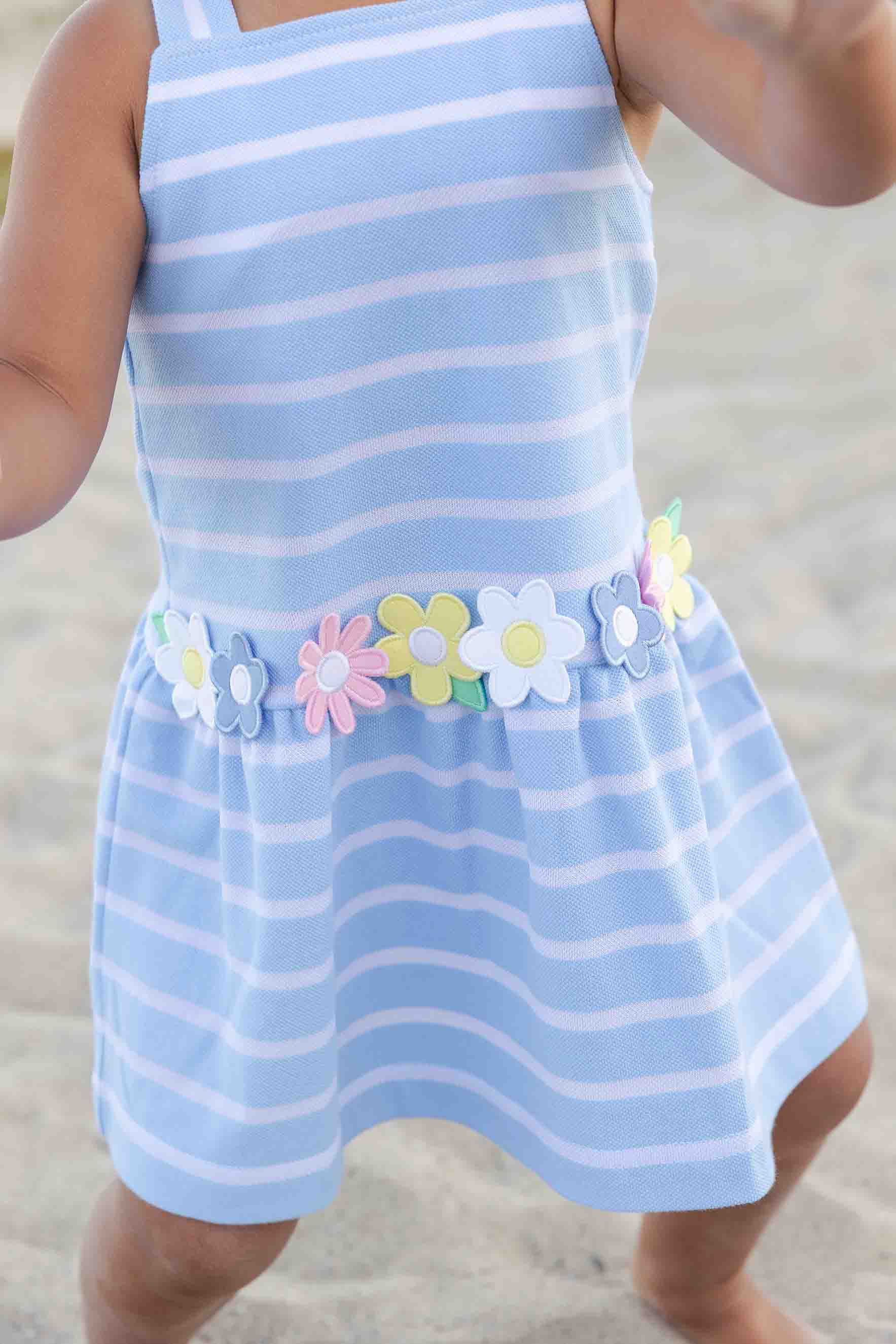 Child wearing a blue and white striped dress with floral decorations on a beach.