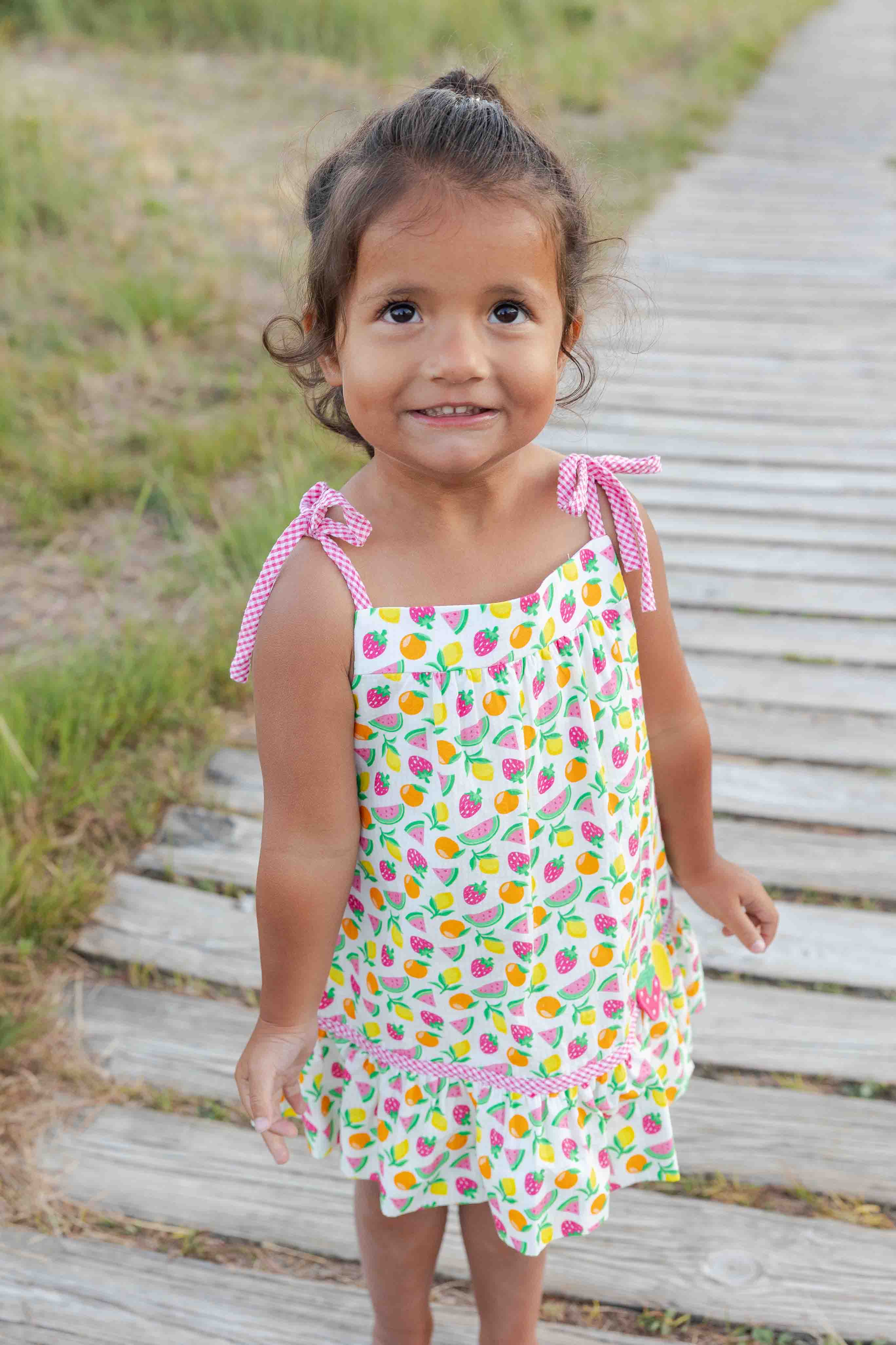 Young girl in a colorful dress standing on a wooden path outdoors