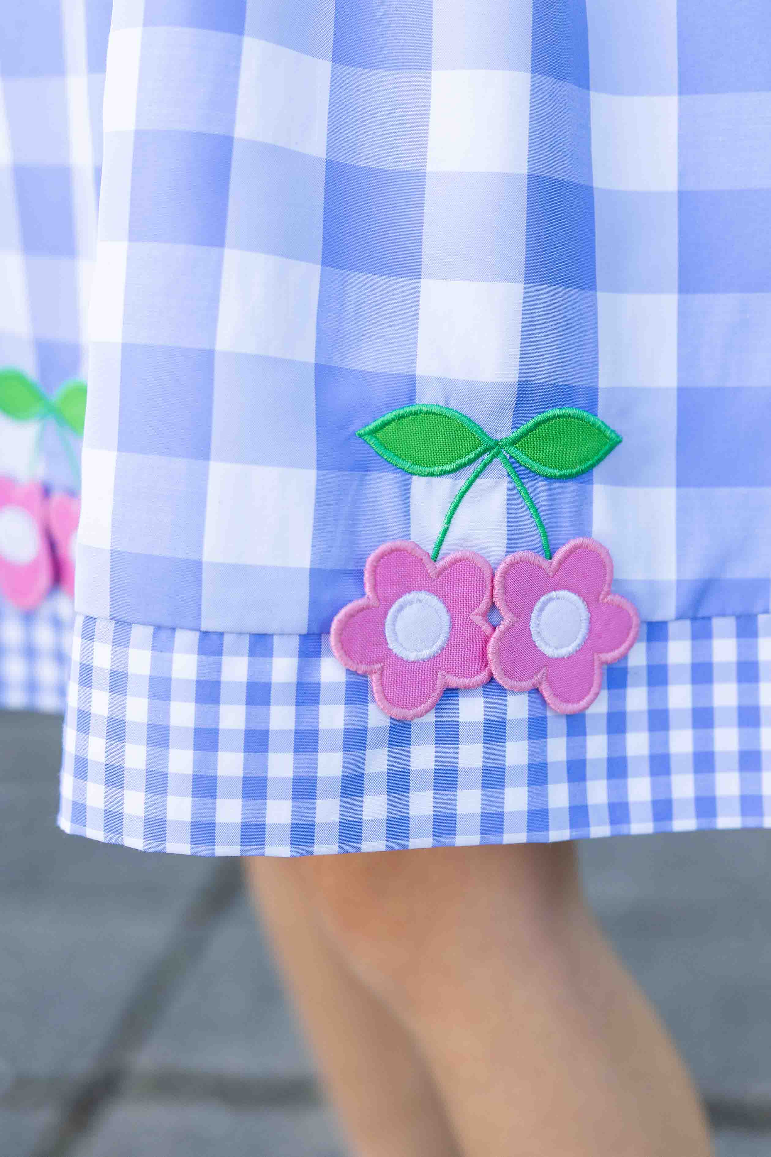 Close-up of a blue and white checkered dress with pink flowers and green leaves.