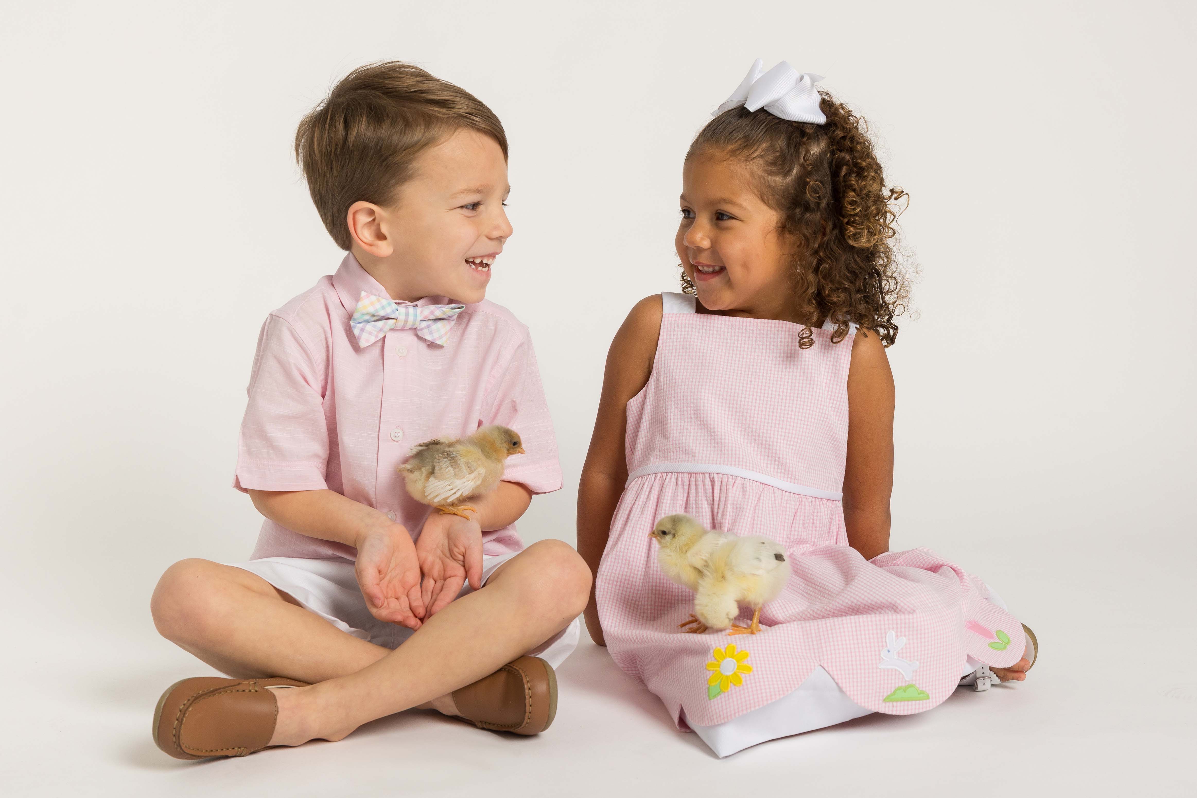 Two children, a boy and a girl, sitting together with baby chicks on a white background.