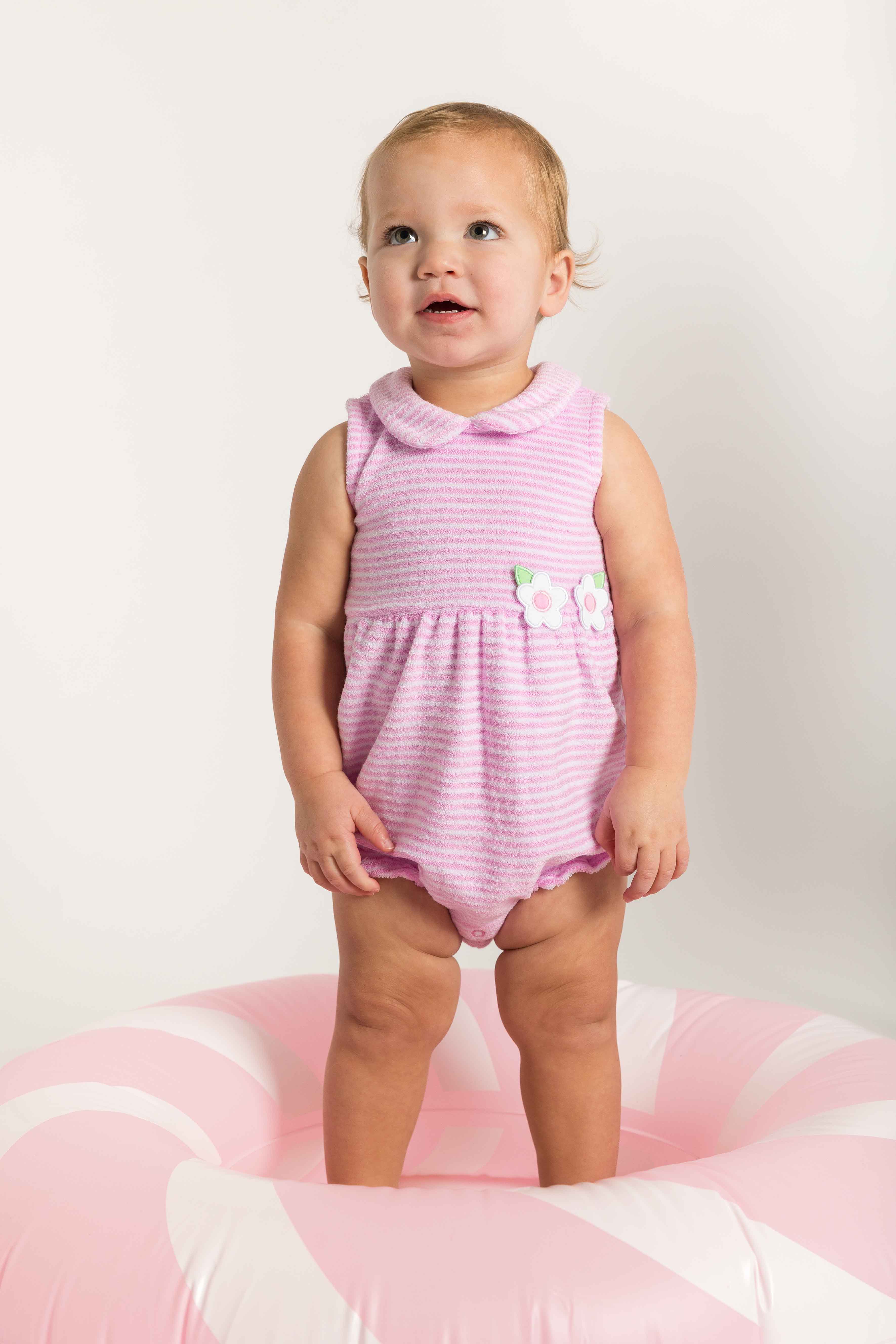 Baby in a pink striped outfit standing on a pink and white striped floatie.