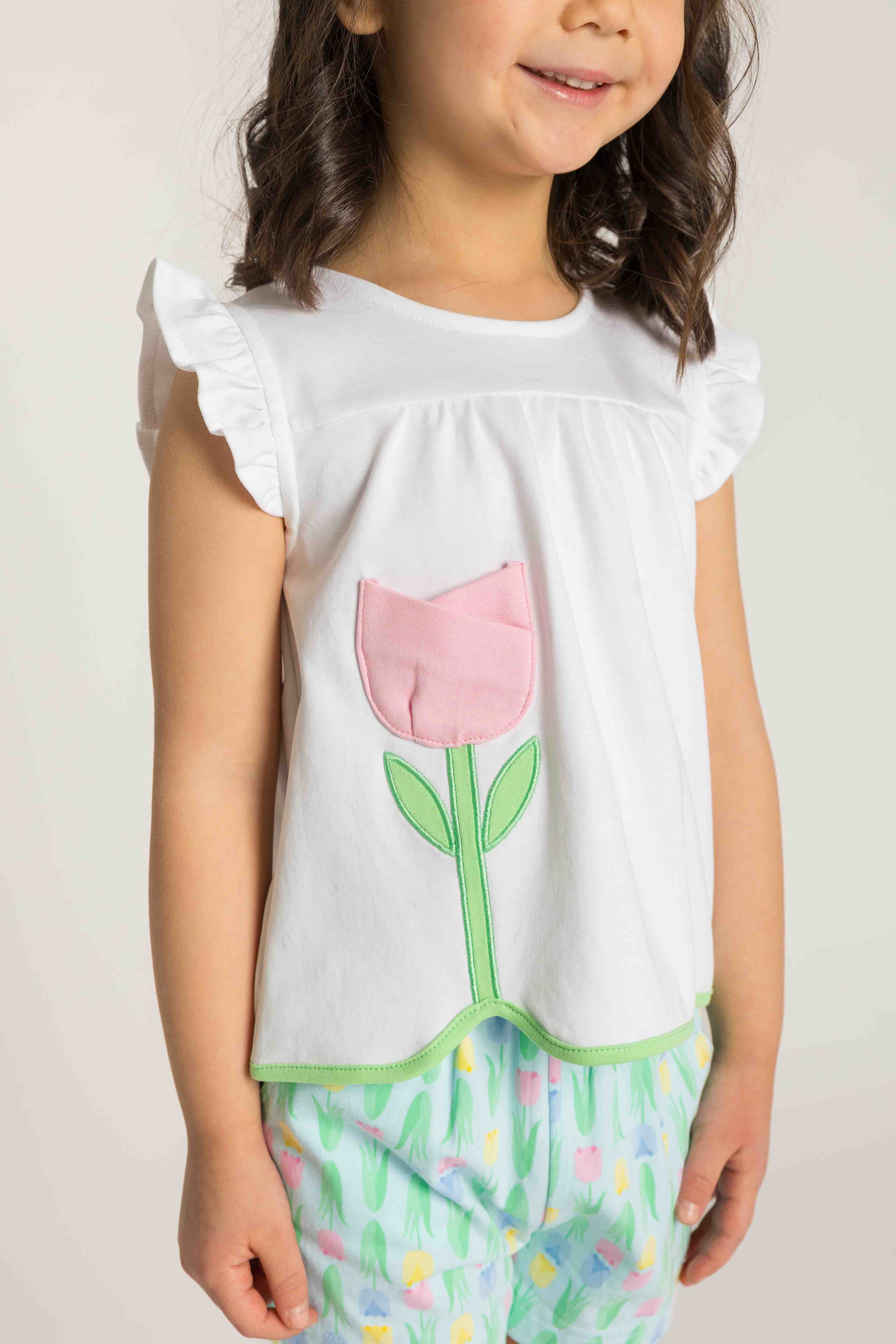 Child wearing a white top with a pink tulip design and colorful pants on a plain background
