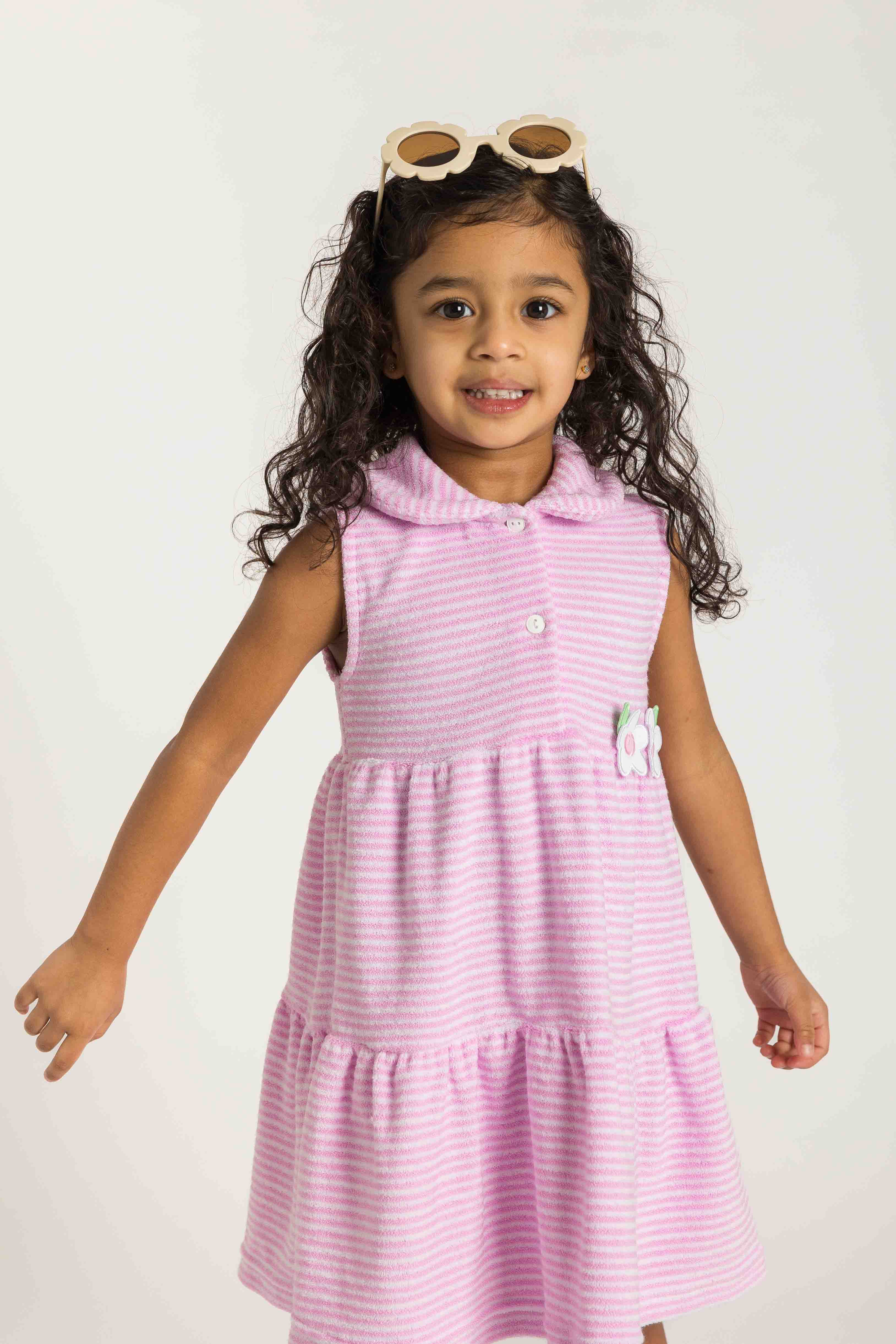 Young girl wearing a pink striped dress with sunglasses on her head against a white background