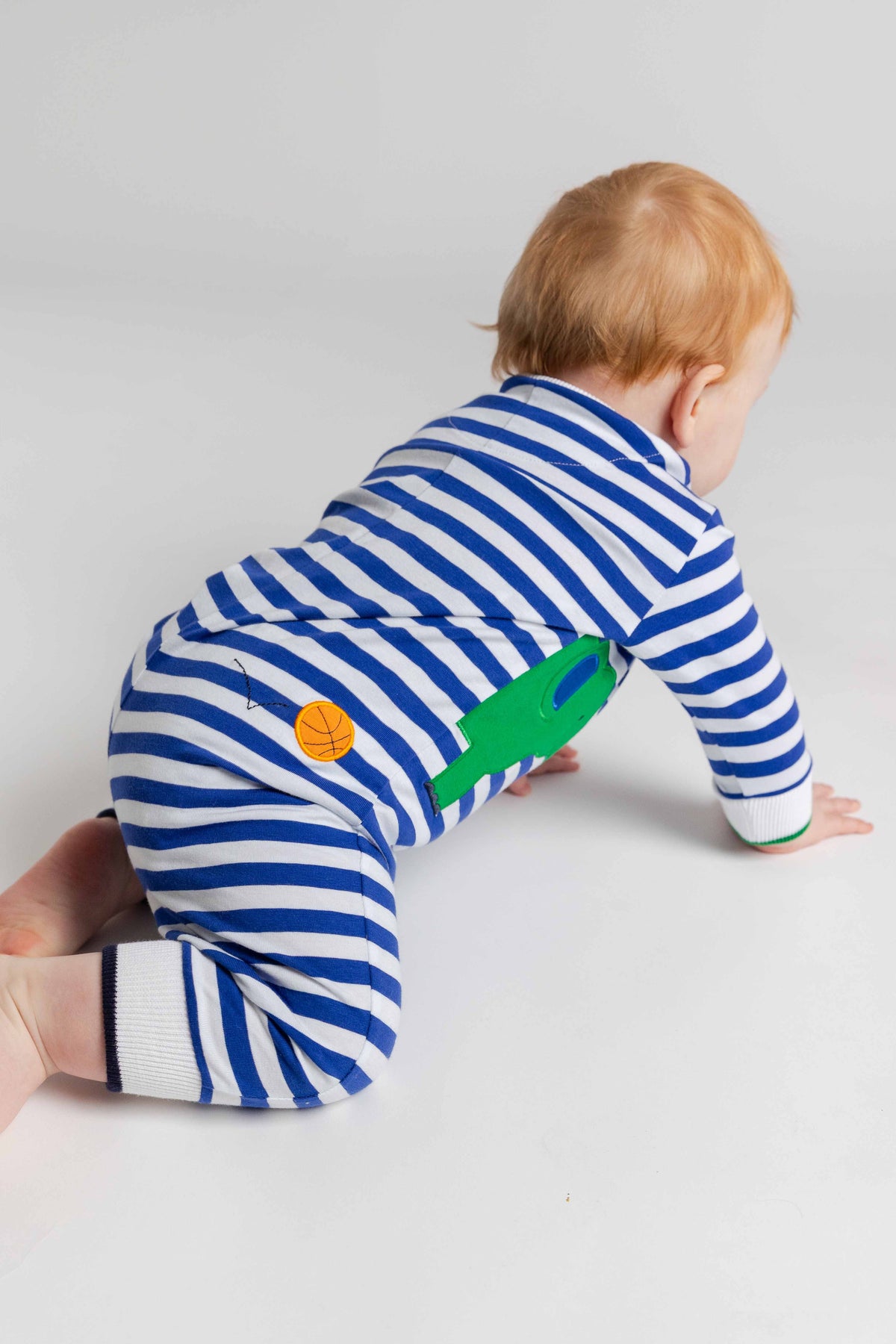 Baby in a blue and white striped outfit with green and orange design on a light gray background