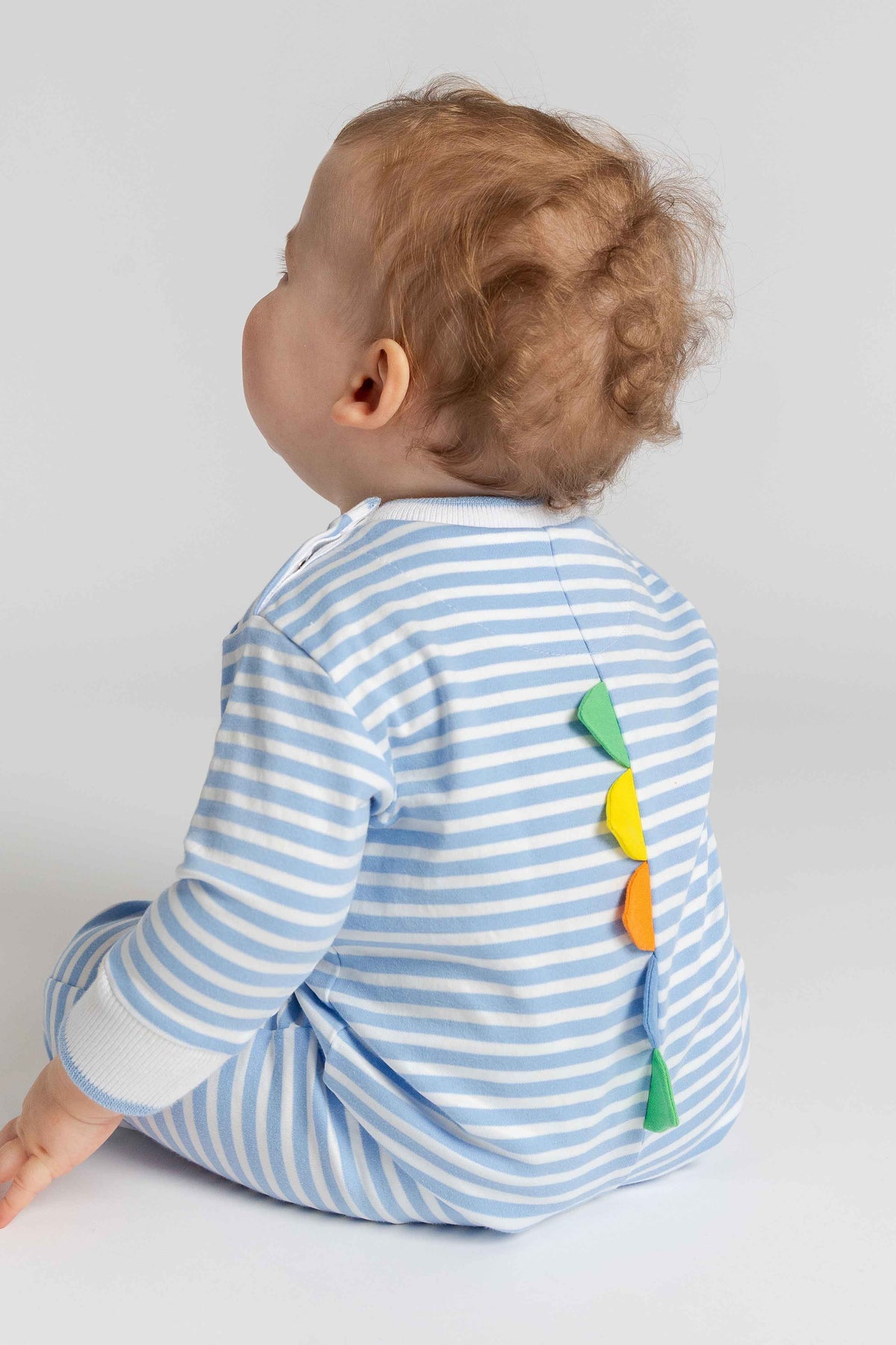 Baby wearing a blue and white striped outfit with colorful leaf design on a light gray background