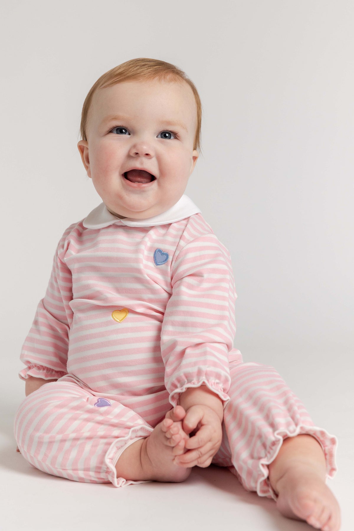 Baby wearing a pink striped outfit with colorful heart buttons on a white background