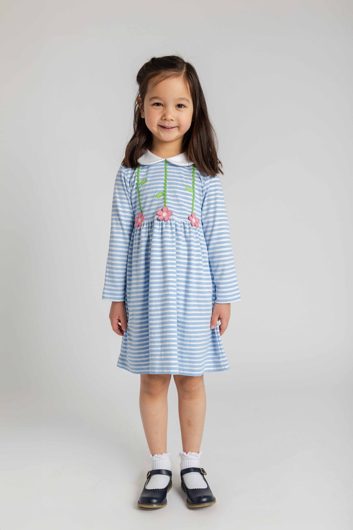 Young girl wearing a blue and white striped dress with floral embroidery on a plain background
