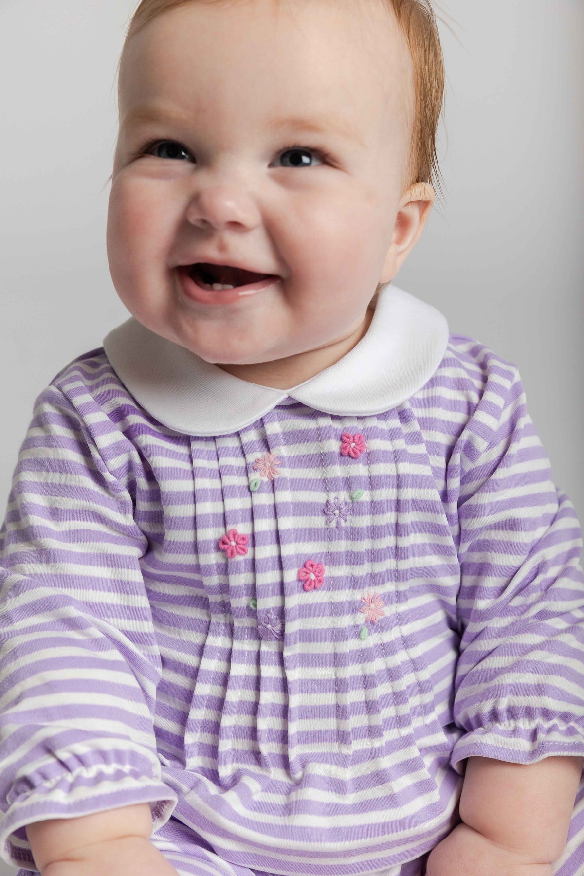 Baby wearing a purple and white striped dress with a white collar on a plain background