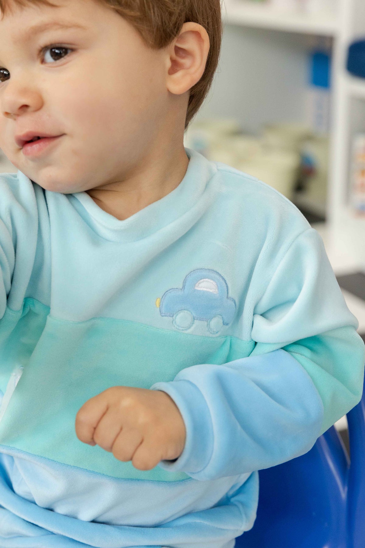 Child wearing a light blue outfit with a car design in a room setting