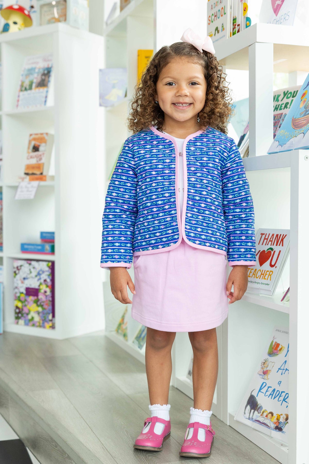 Young girl in a blue jacket and pink skirt standing in a store.