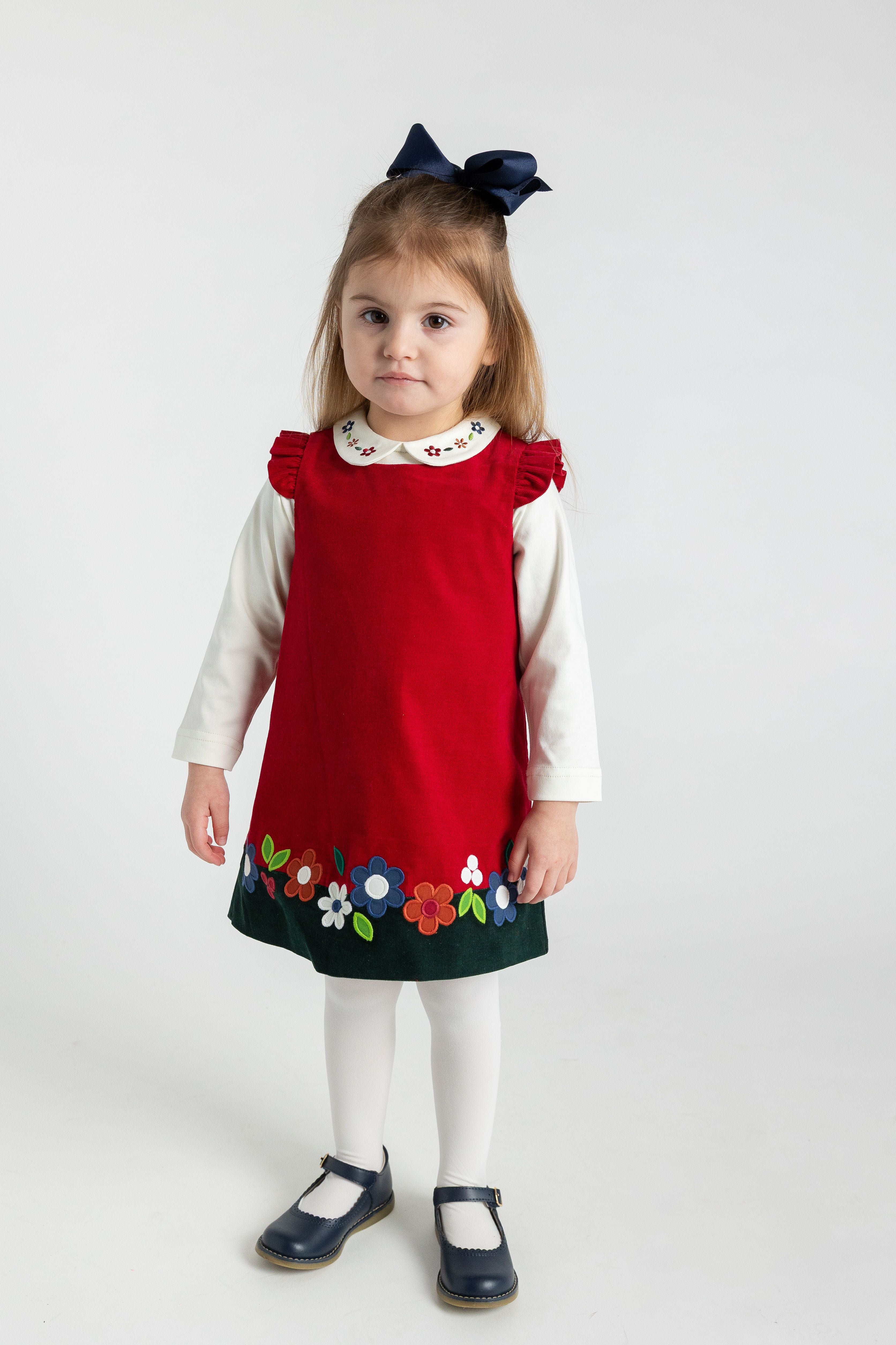 Young girl wearing a red dress with floral patterns on a white background