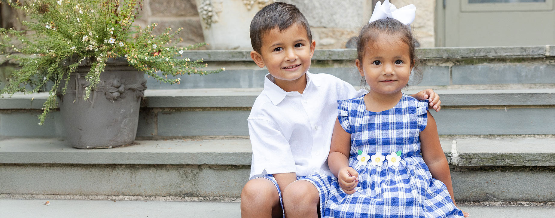 young brother and sister sitting on steps in blue plaid outfits