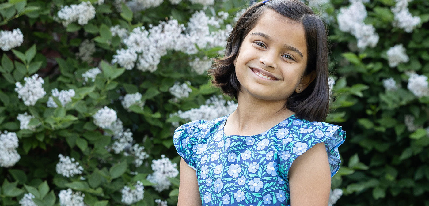 Tween girl in floral print dress in front of floral bush