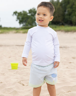 toddler boy on beach in seersucker trunk and white rashguard