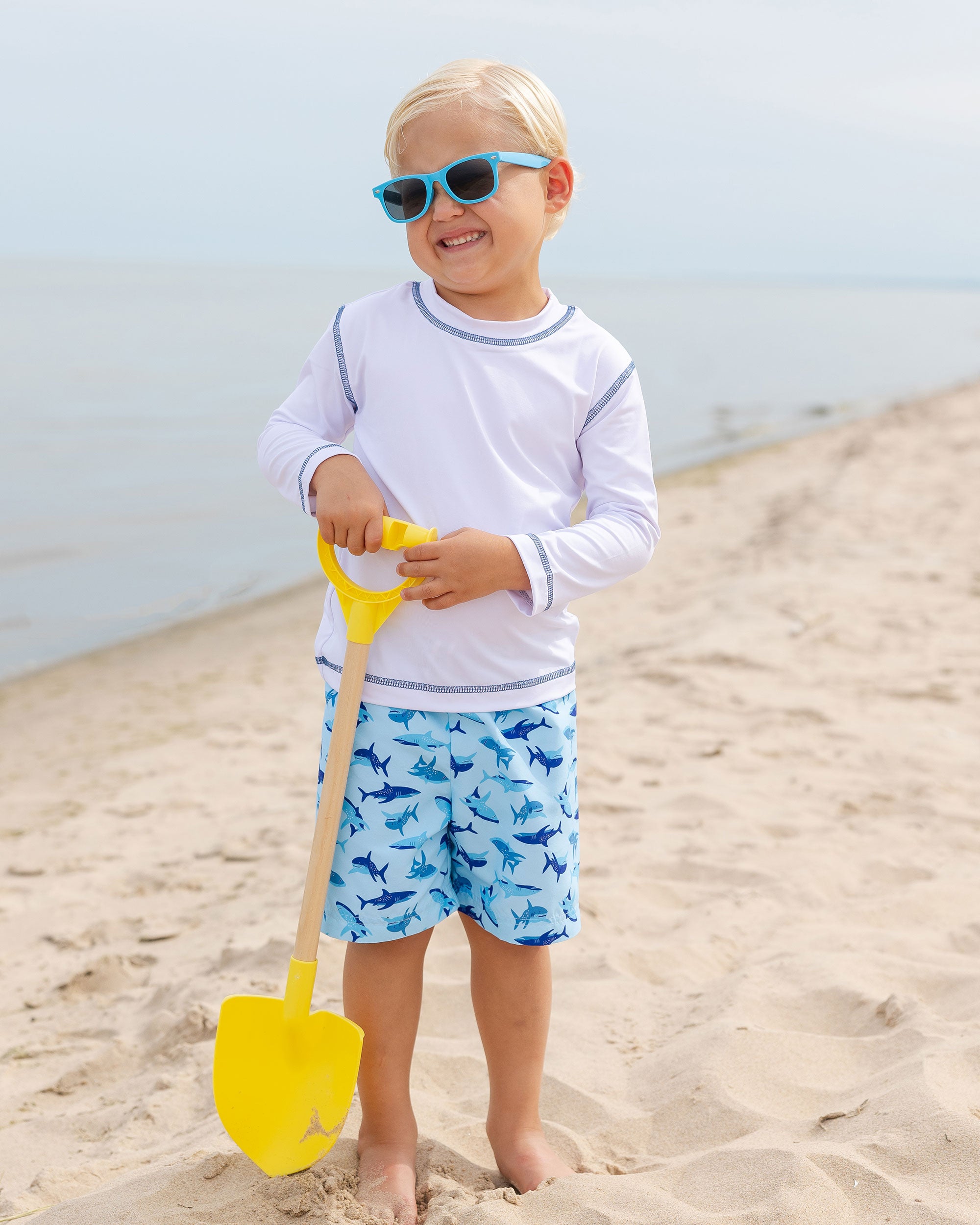 young boy on beach in swim trunks with sharks