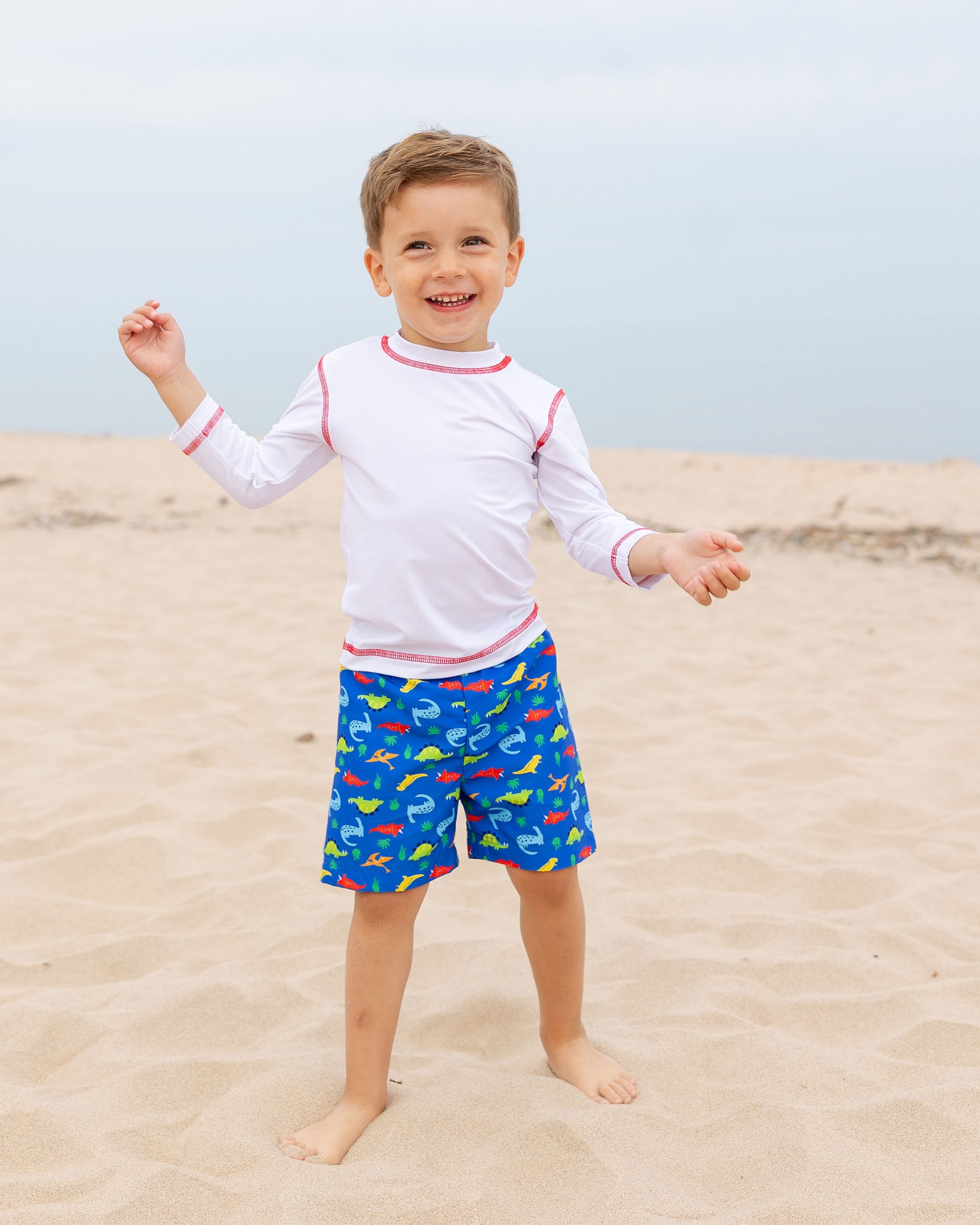 boy at beach wearing swim trunk with dinosaurs